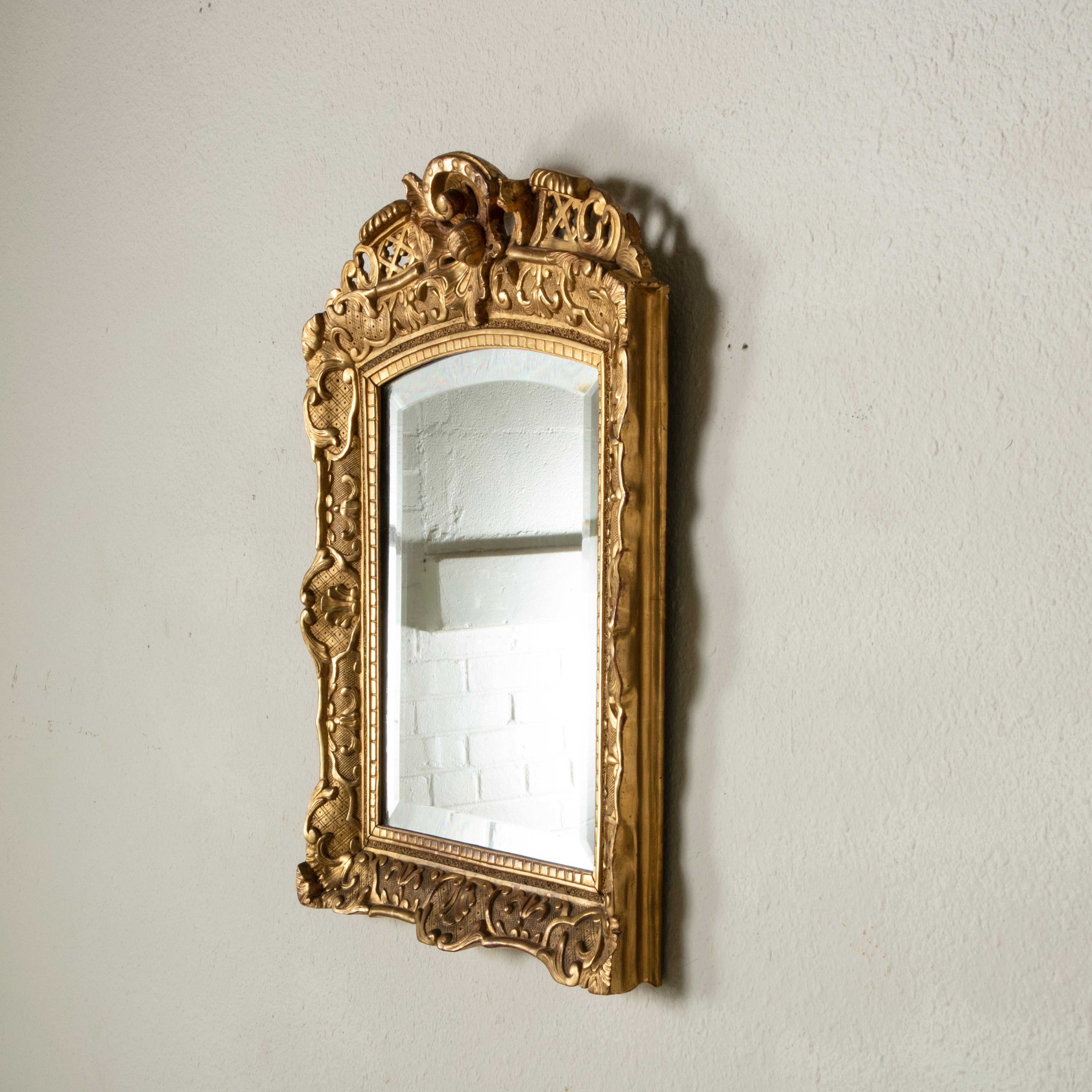 This French giltwood mirror reflects the Louis XV and Regency styles as interpreted in the late nineteenth century and is fitted with beveled glass. The mirror features intricate scrolling and an asymmetrical flourish at the top. Leaves and shells