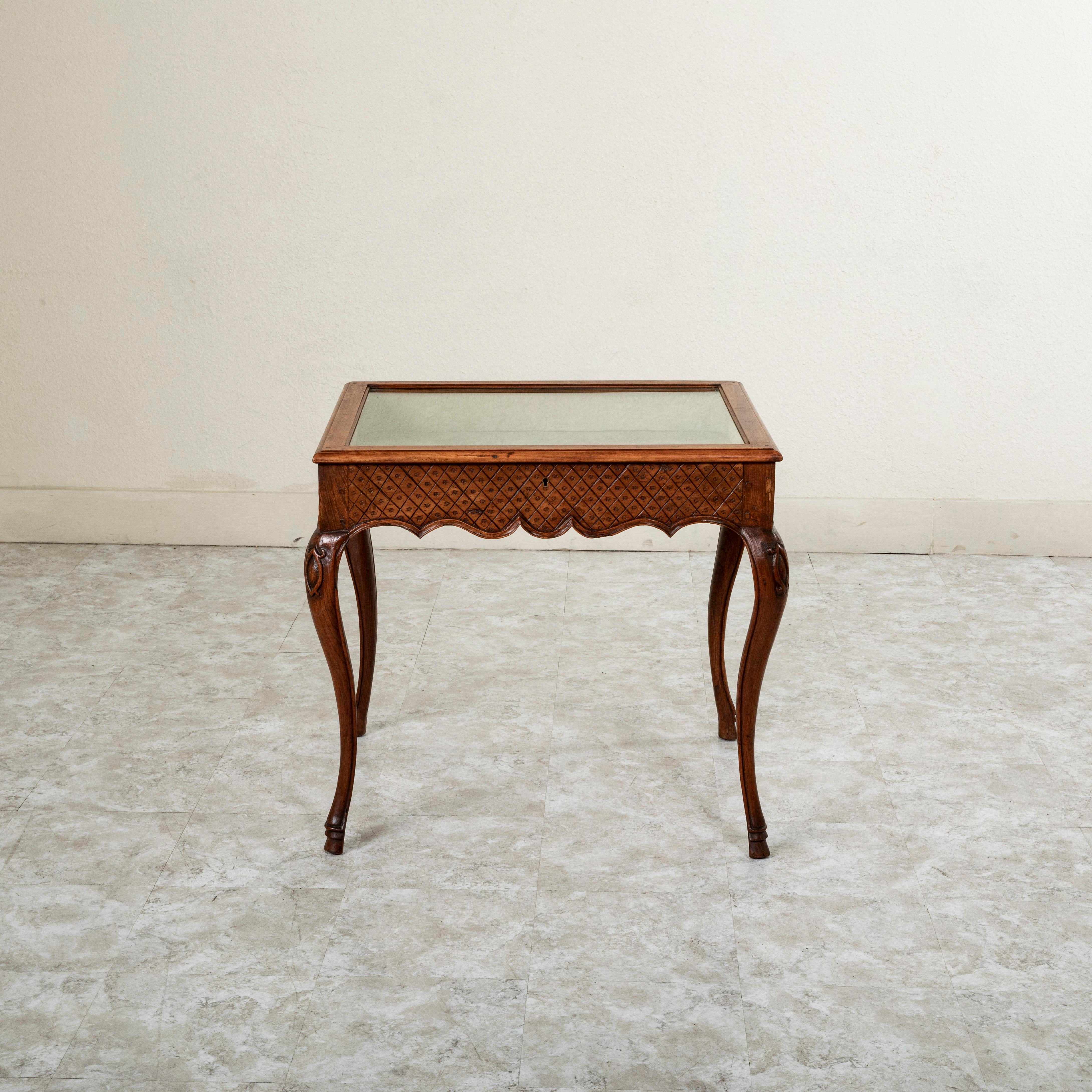This late nineteenth century French Regency style hand pegged walnut display table features hand carved detailing of a diamond pattern on all sides. The hinged glass top opens for access to its fabric lined interior. The table rests on classic