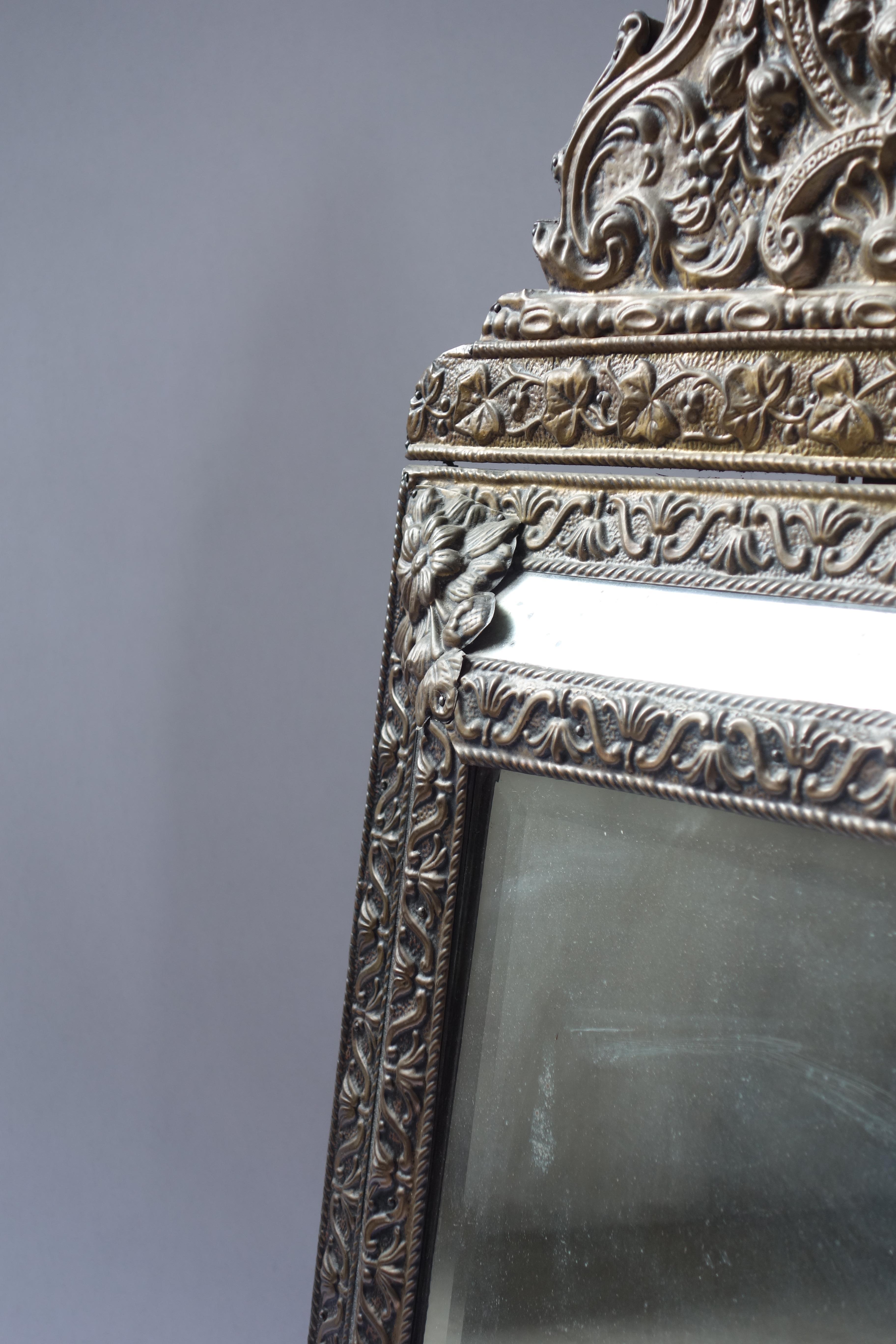 Beautifully crafted late 19th century French wall mirror featuring an ornate repoussé brass frame created through the traditional repoussé metalworking technique. The frame's brass surface has developed a soft, aged patina adding depth and enhancing