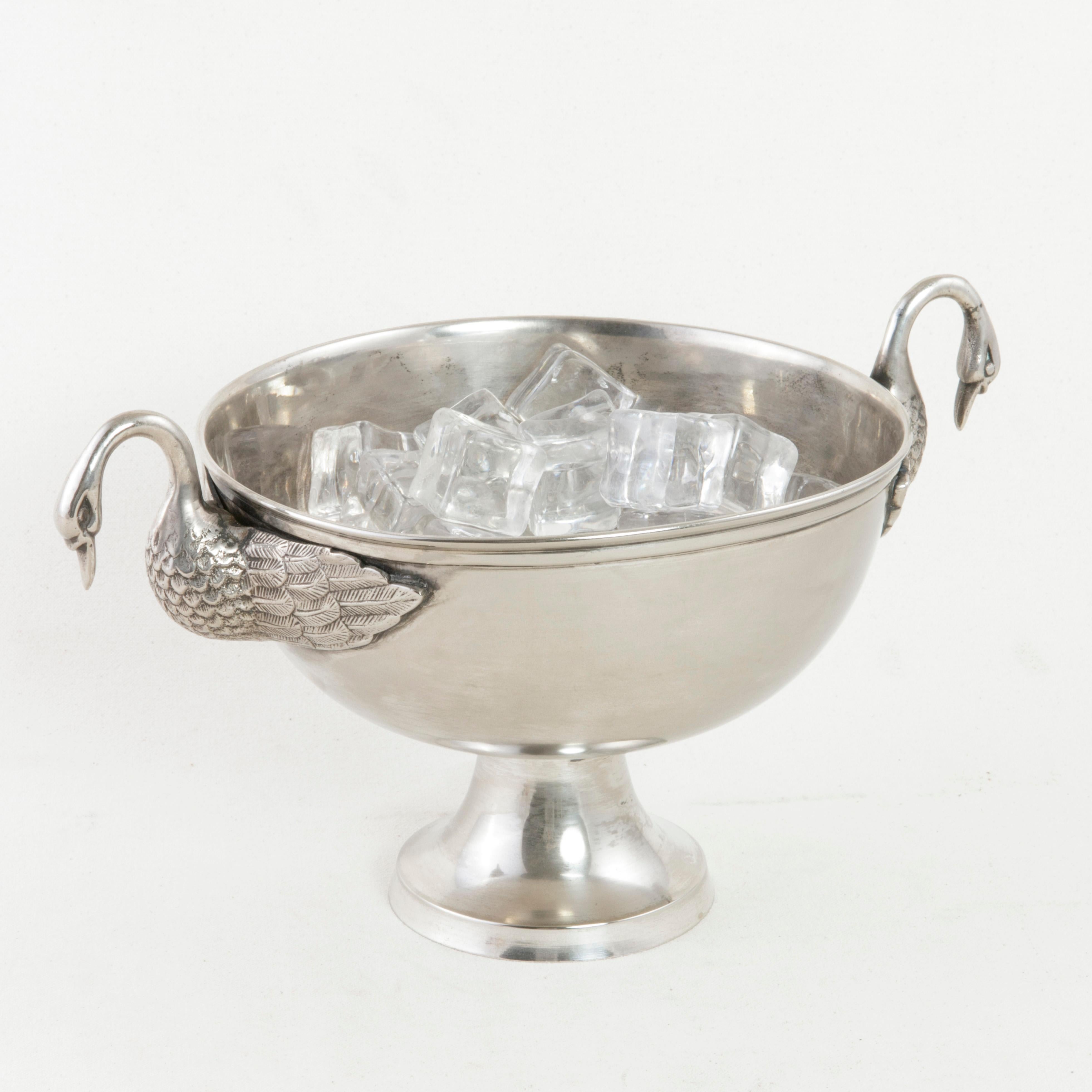This late 19th century French Restauration style ice bucket features two handles formed by swans with wings spread. Resting on a footed base, the diameter of the bowl measures 8 inches. This piece is sure to make a statement when entertaining guests