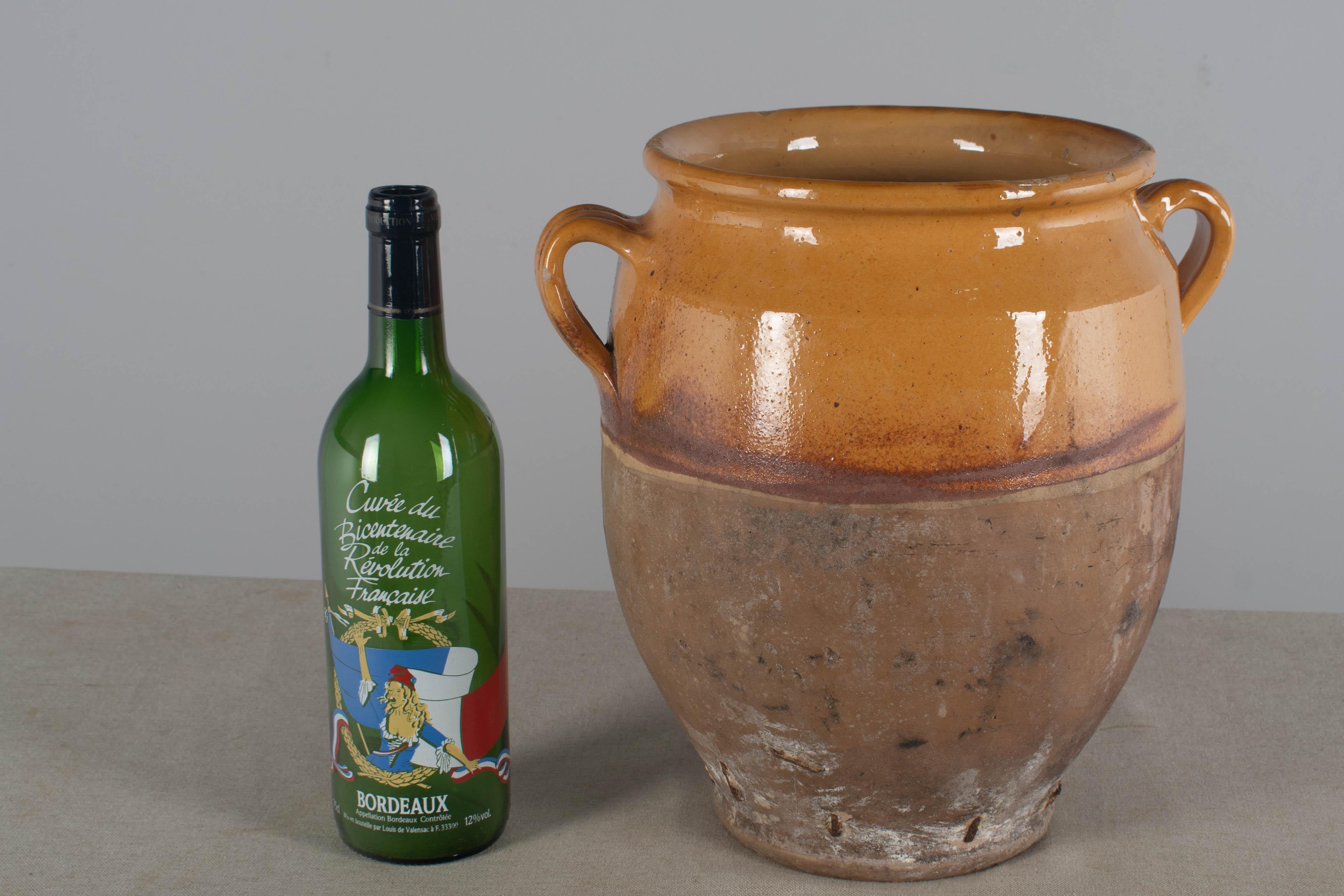 A late 19th century  earthenware confit pot from the Southwest of France with traditional yellow ochre glaze.  Chips and losses to glaze, hairline crack near top. Notice the old restoration at the base using staples. Sign of an old pottery.  These