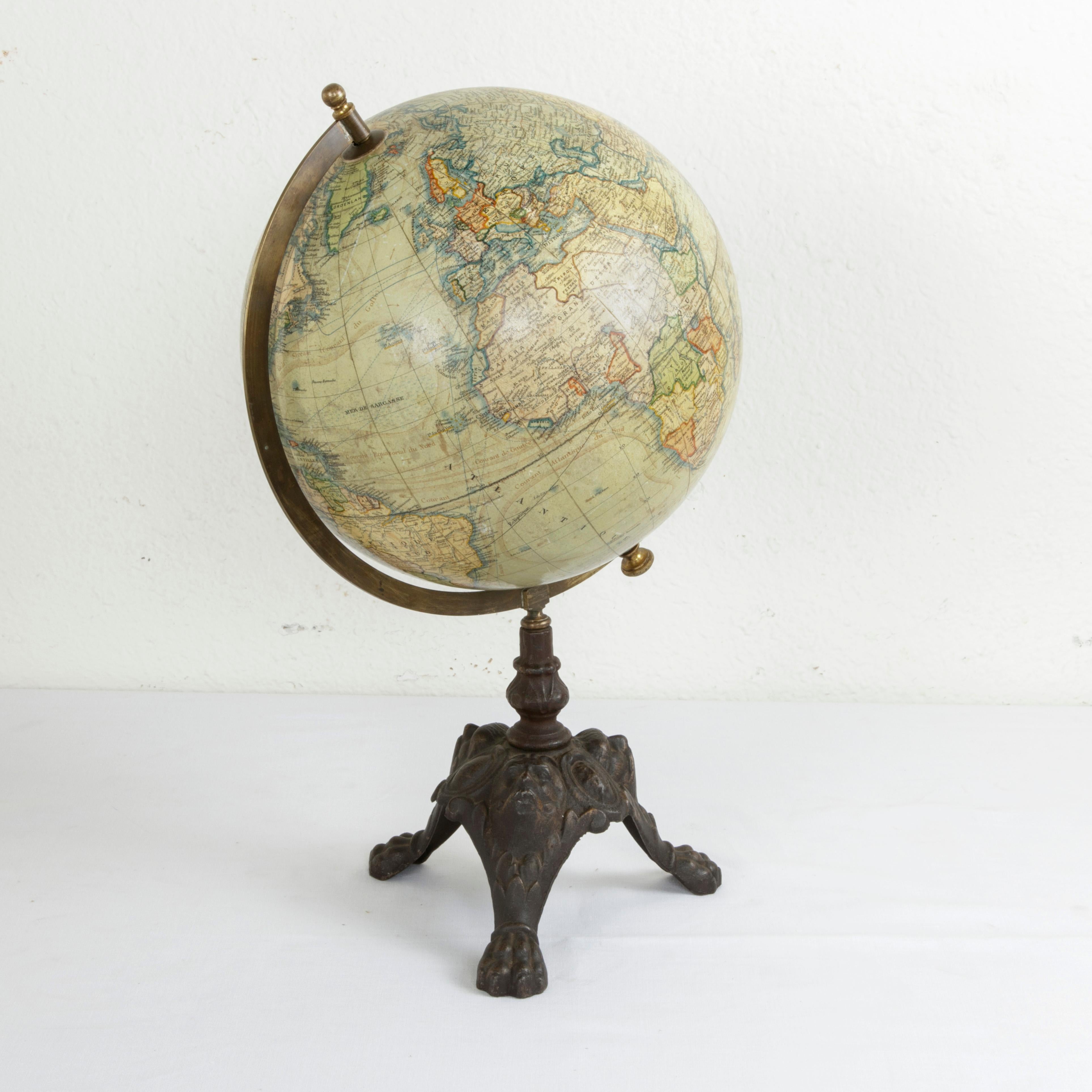 This late 19th century terrestrial globe features its original cast iron tripod base with claw feet, masques, and cartouches. Displaying the world as it was around the turn of the 20th century, this globe was created by the Belgian cartographer