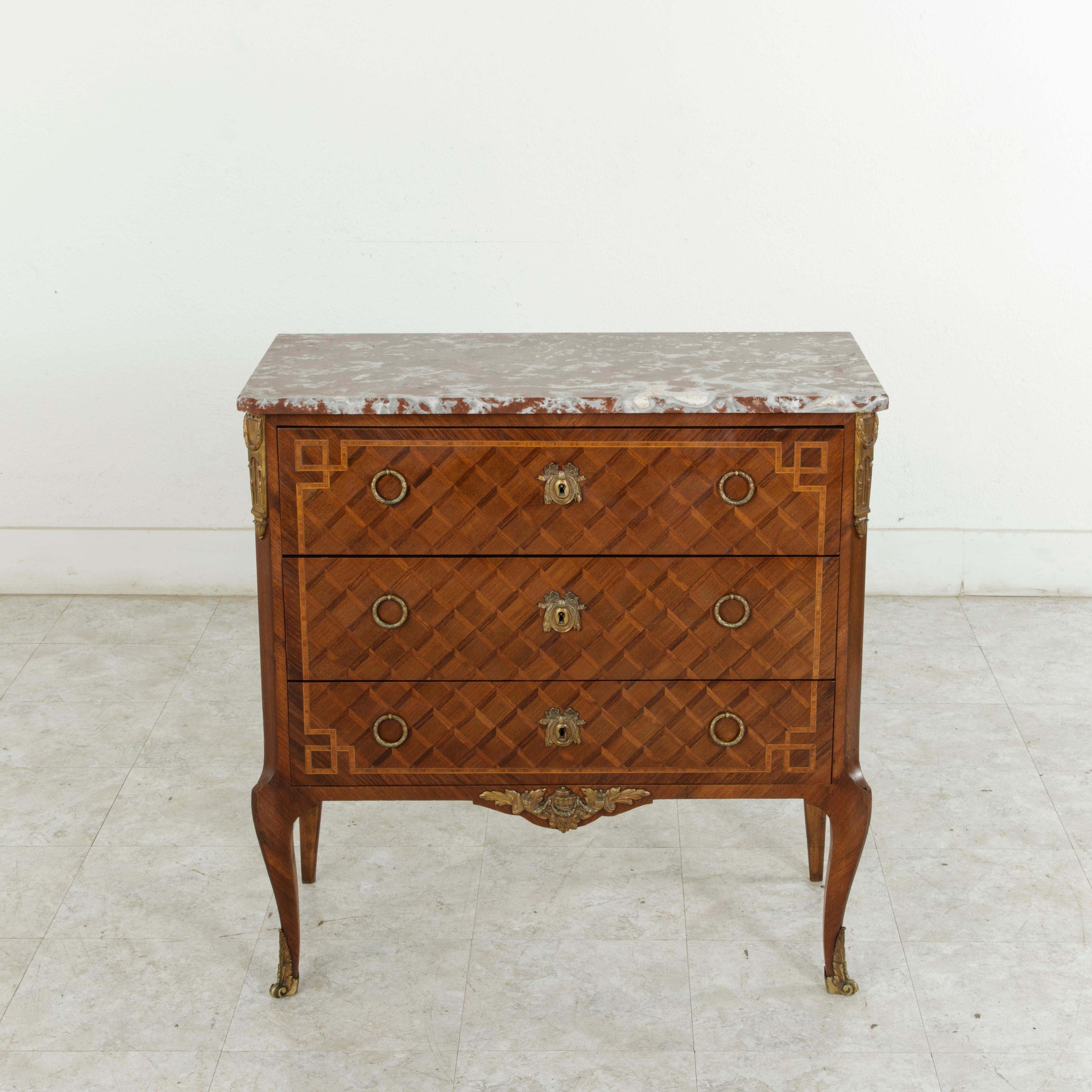 This late 19th century Louis XV-Louis XVI transition style chest features a rosewood and walnut marquetry facade in a geometric diamond pattern and is finished with a griotte marble top. Bronze ormolu detailed with hanging garlands are mounted on