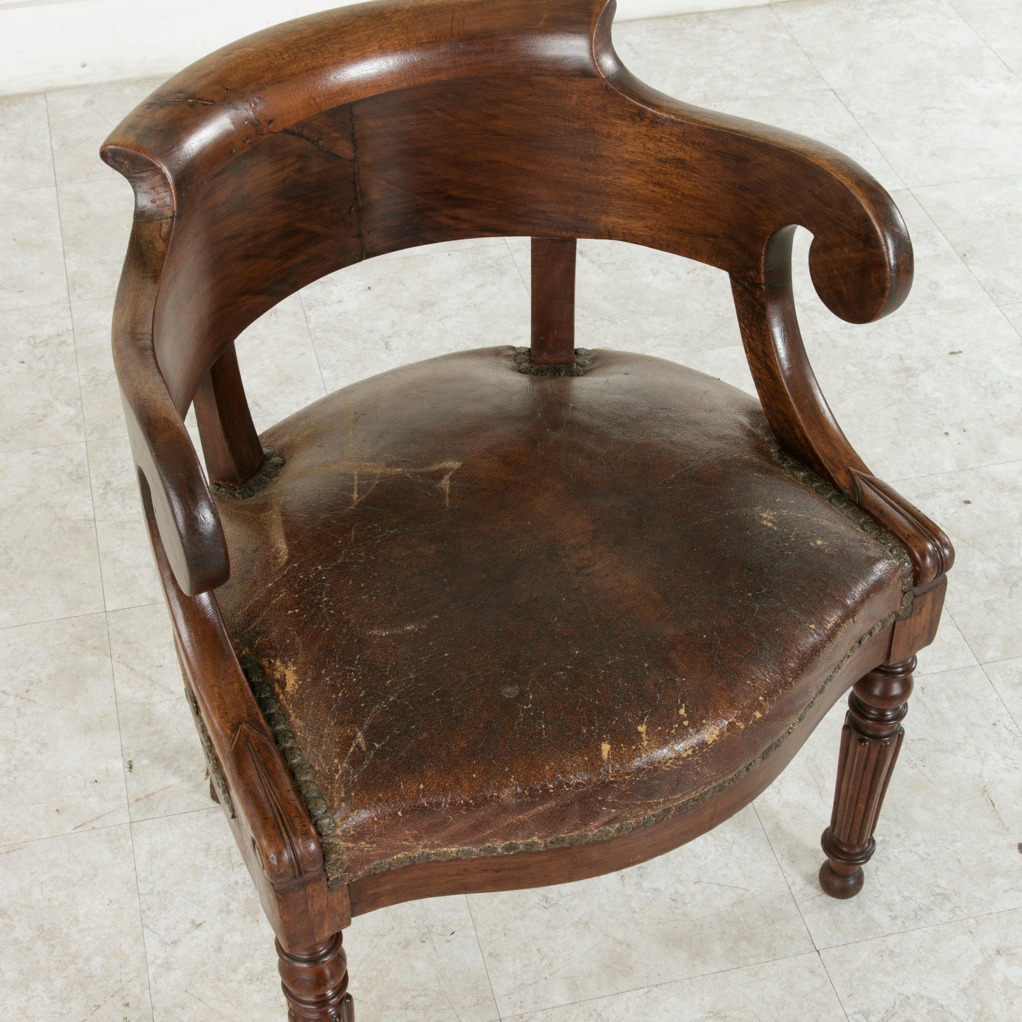 This late 19th century French walnut armchair or bergere features a curved back with scrolled armrests and two turned front legs with inverted fluting. The back legs sweep back, a look referred to as 