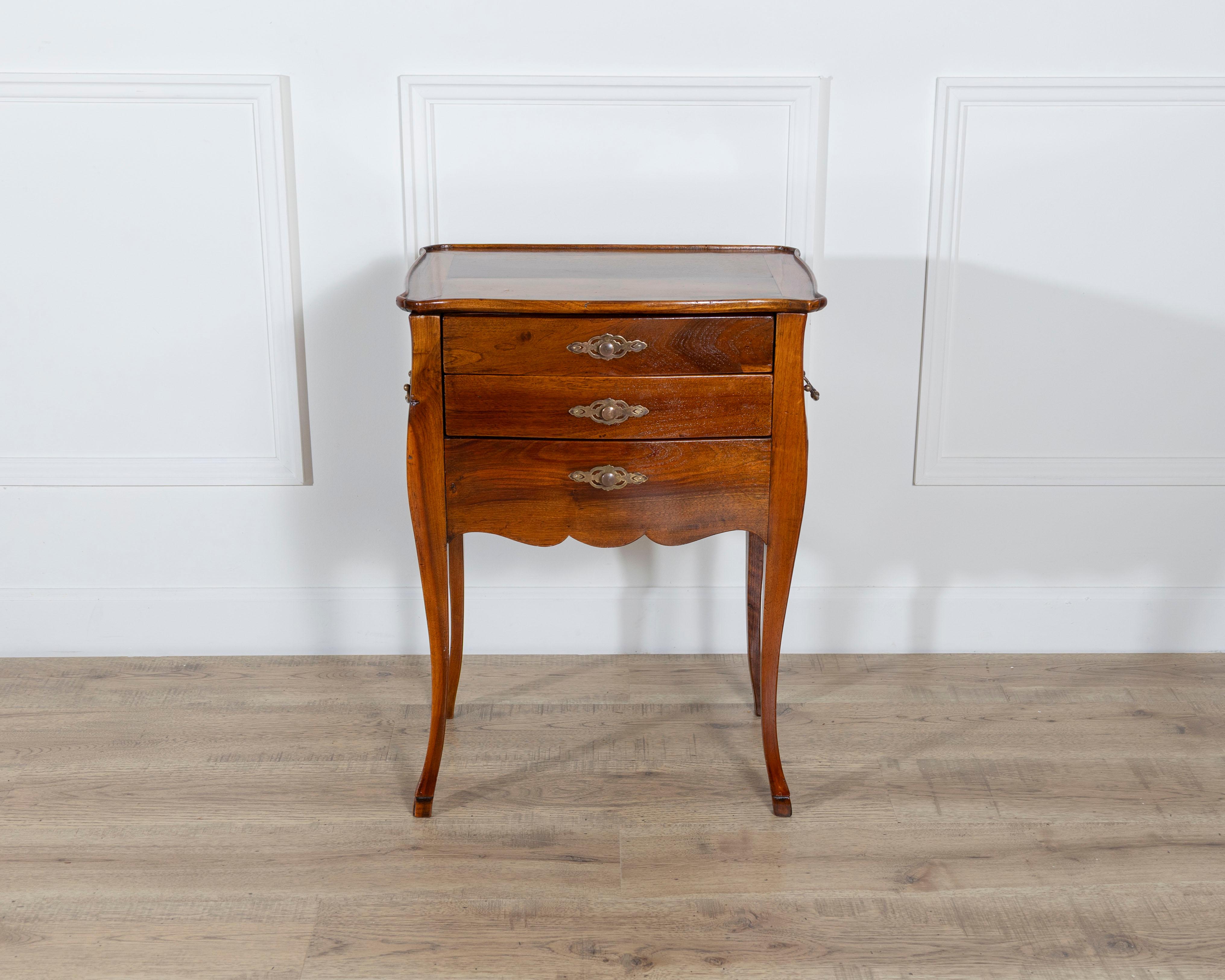 A refined late 19th-century cabinet or bedside table crafted in rich walnut, featuring a delicate writing desk function. The elegant serpentine front is fitted with three drawers, each adorned with finely cast brass pulls and escutcheons that