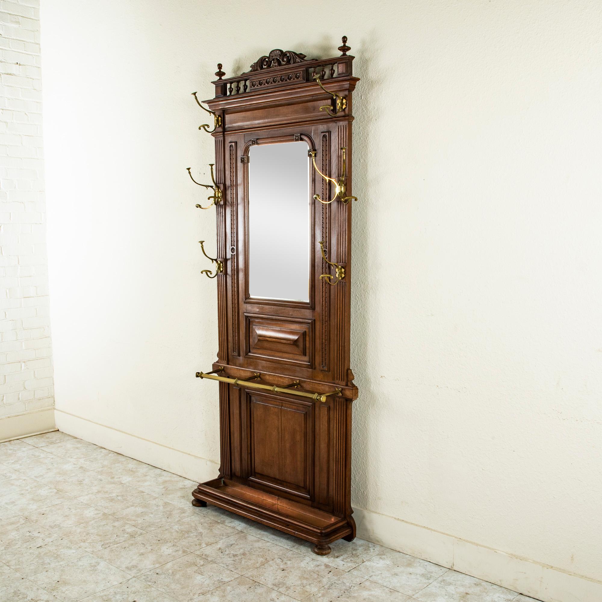 This late nineteenth century Henri II style hall tree is constructed of solid walnut with eight bronze hooks and its original beveled mirror and is detailed with fluting on the sides, a stylized leaf and rosette pattern and an upper banister