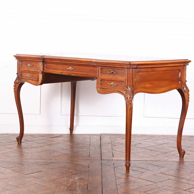 A late-19th century French carved walnut Louis XV style breakfront ‘bureau plat’ or writing desk. Fitted with five drawers to the frieze and with newly-installed gilt tooled leather surfaces to the top and two pull-outs on each side. Carved and