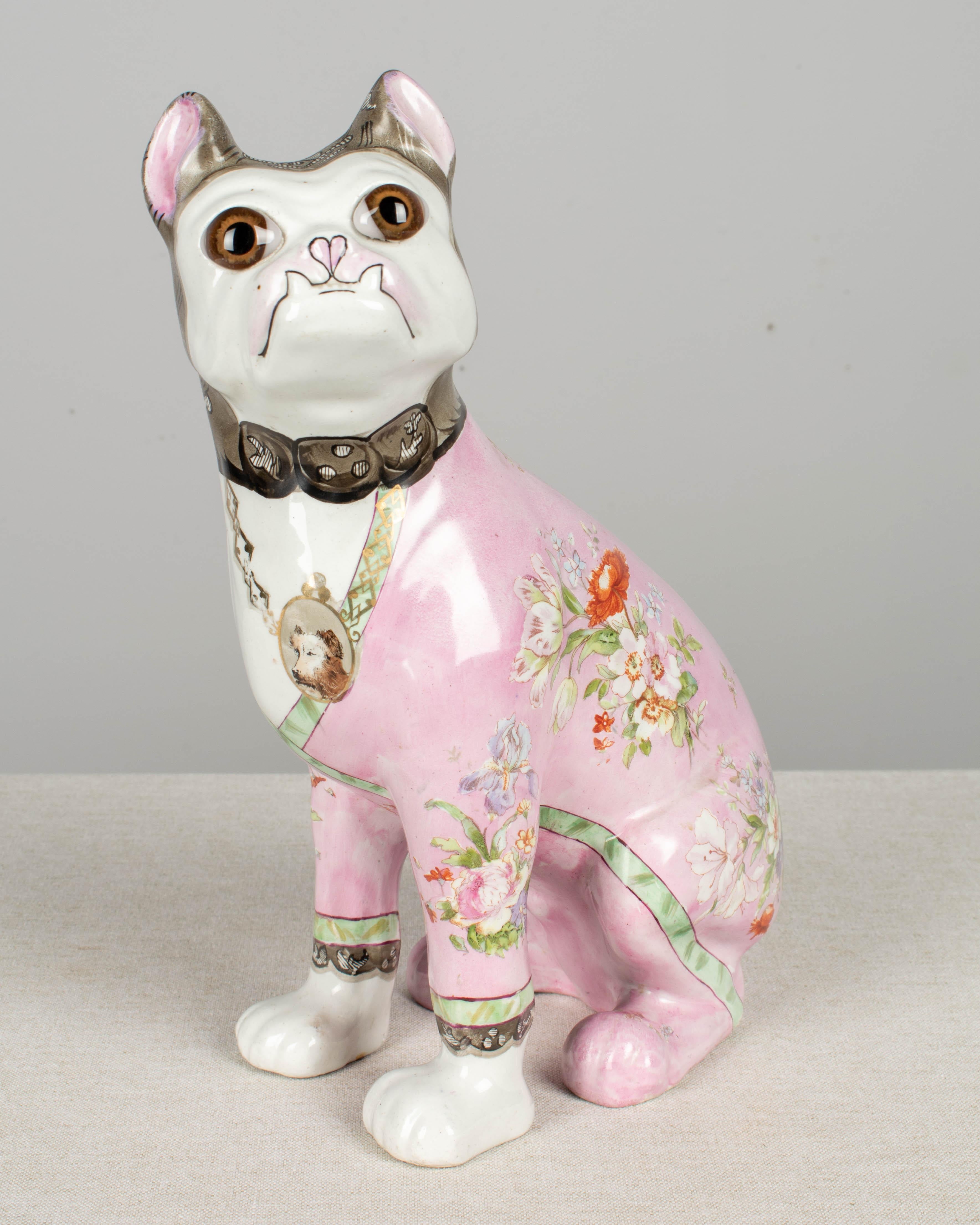 A French faience dog sculpture by Art Nouveau artist Emile Galle (1846-1904). A whimsical ceramic figure of a seated pug or French bulldog, with glass eyes, hand painted with ornate decoration consisting of a lily motif at the back of the head and