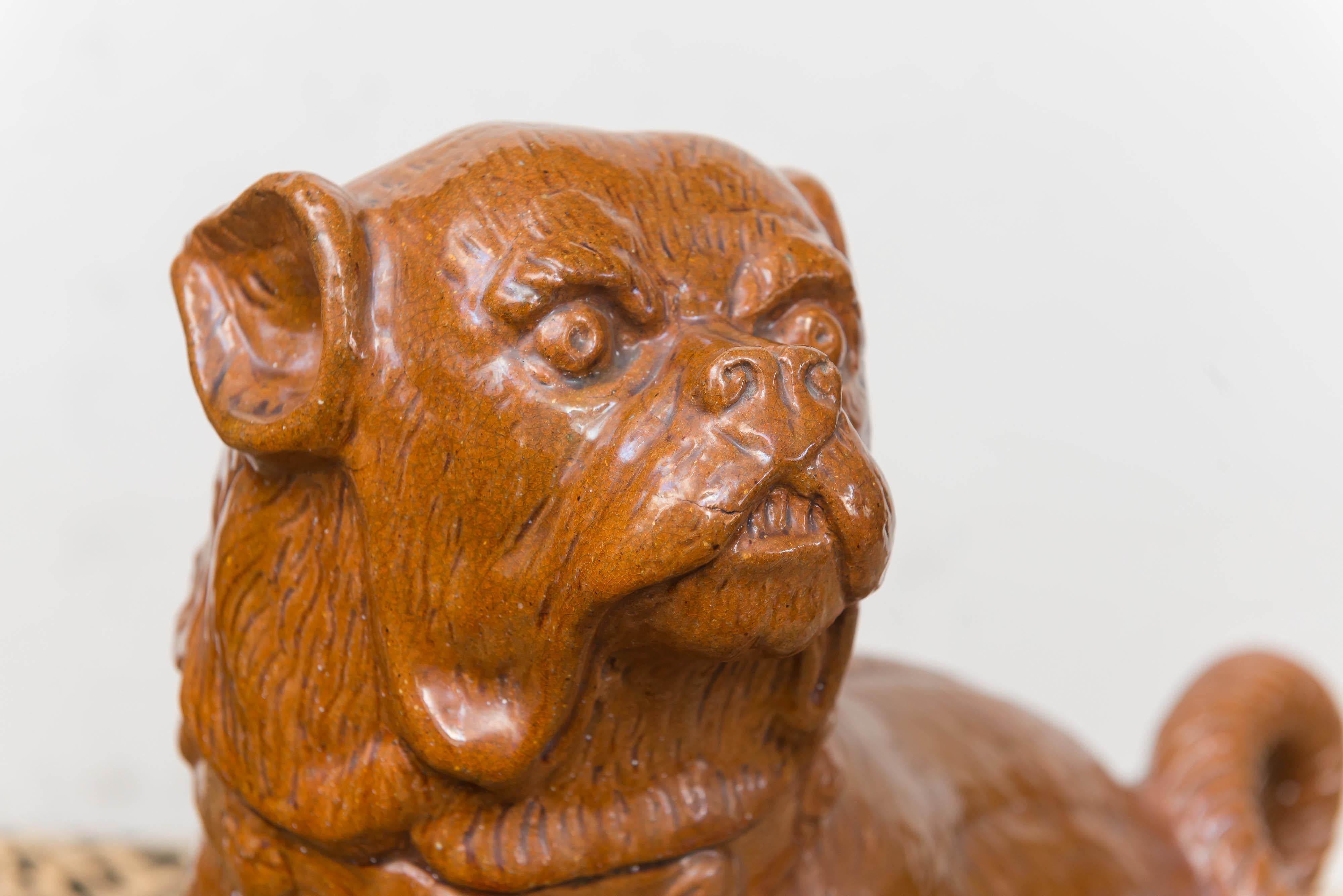 Late 19th century German pug dog. Heavy terracotta with brown carmel color glaze.
Seated, with the head turned, in active pose. Good confirmation and details of the face, ears, coiled tail with a bold collar. The base in the form of a cushion with