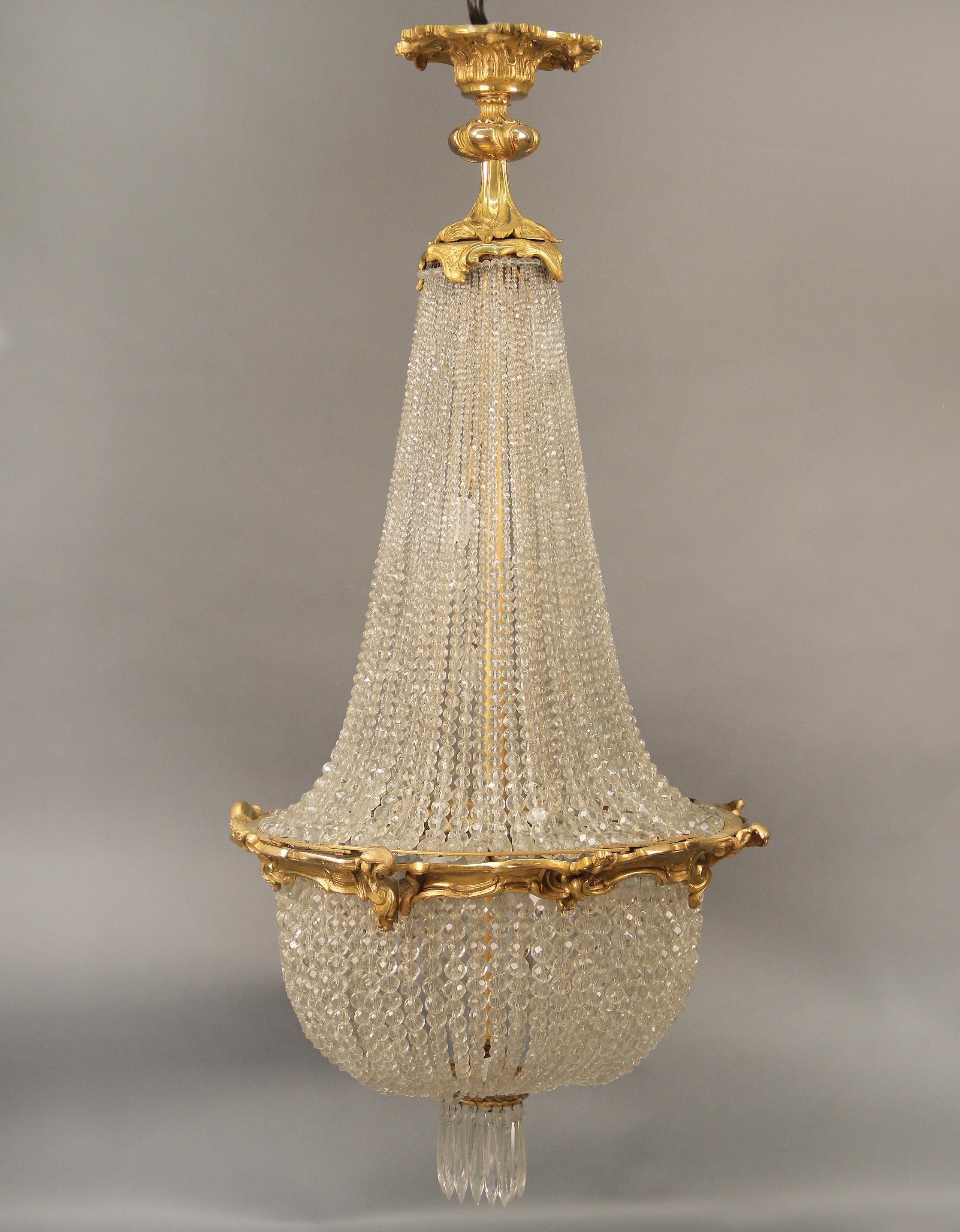 A Late 19th Century Gilt Bronze and Crystal Seven Light Basket Chandelier

The large bronze crown with flowing beads leading down to a basket with drop crystals, seven tiered interior lights.