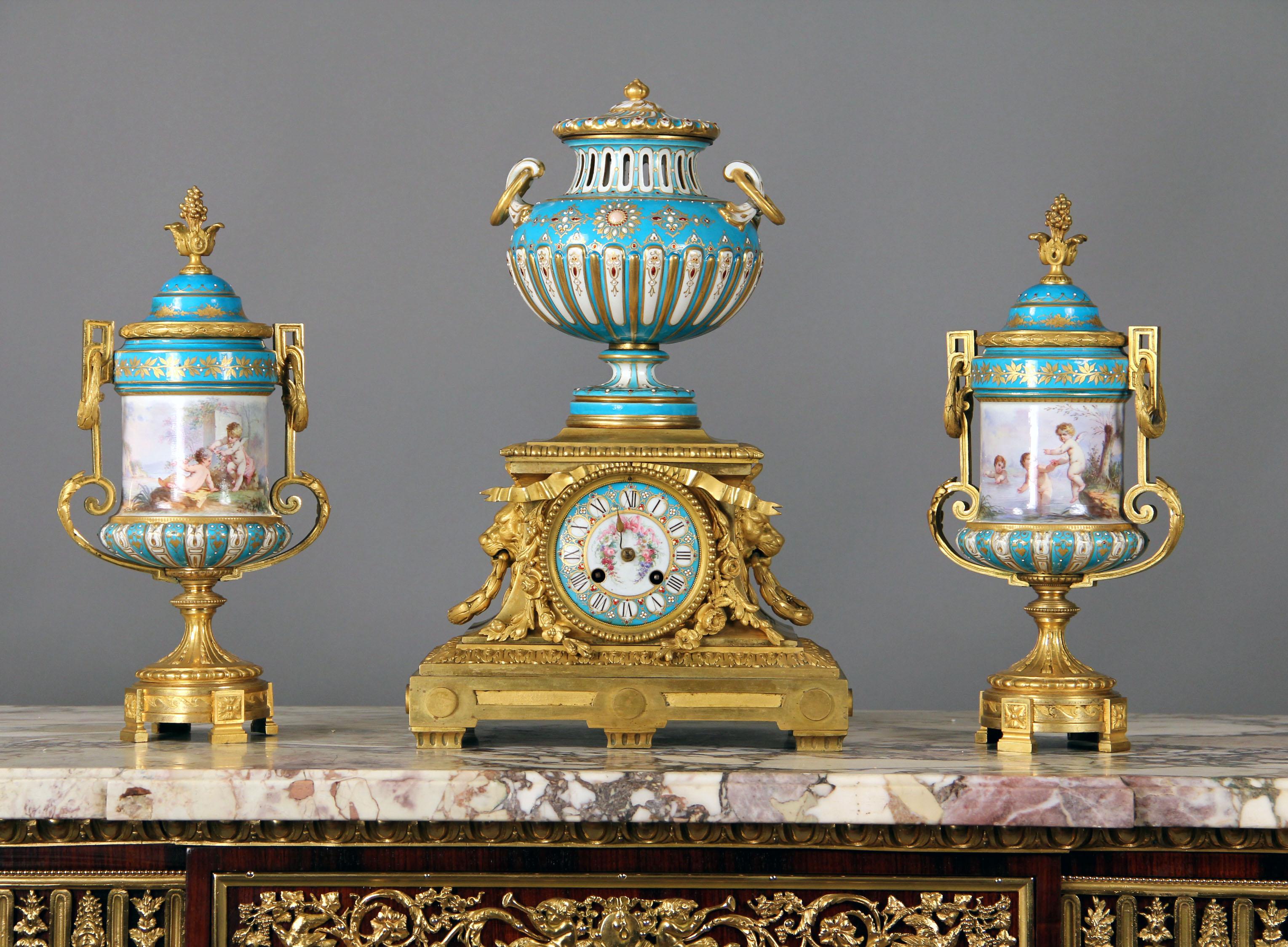 Late 19th century gilt bronze and turquoise Sèvres porcelain 'Jeweled' three-piece clock set

The clock surmounted by a covered urn, the clock case flanked by lion masks, en suite with a pair of vases with putti playing near water.

In late