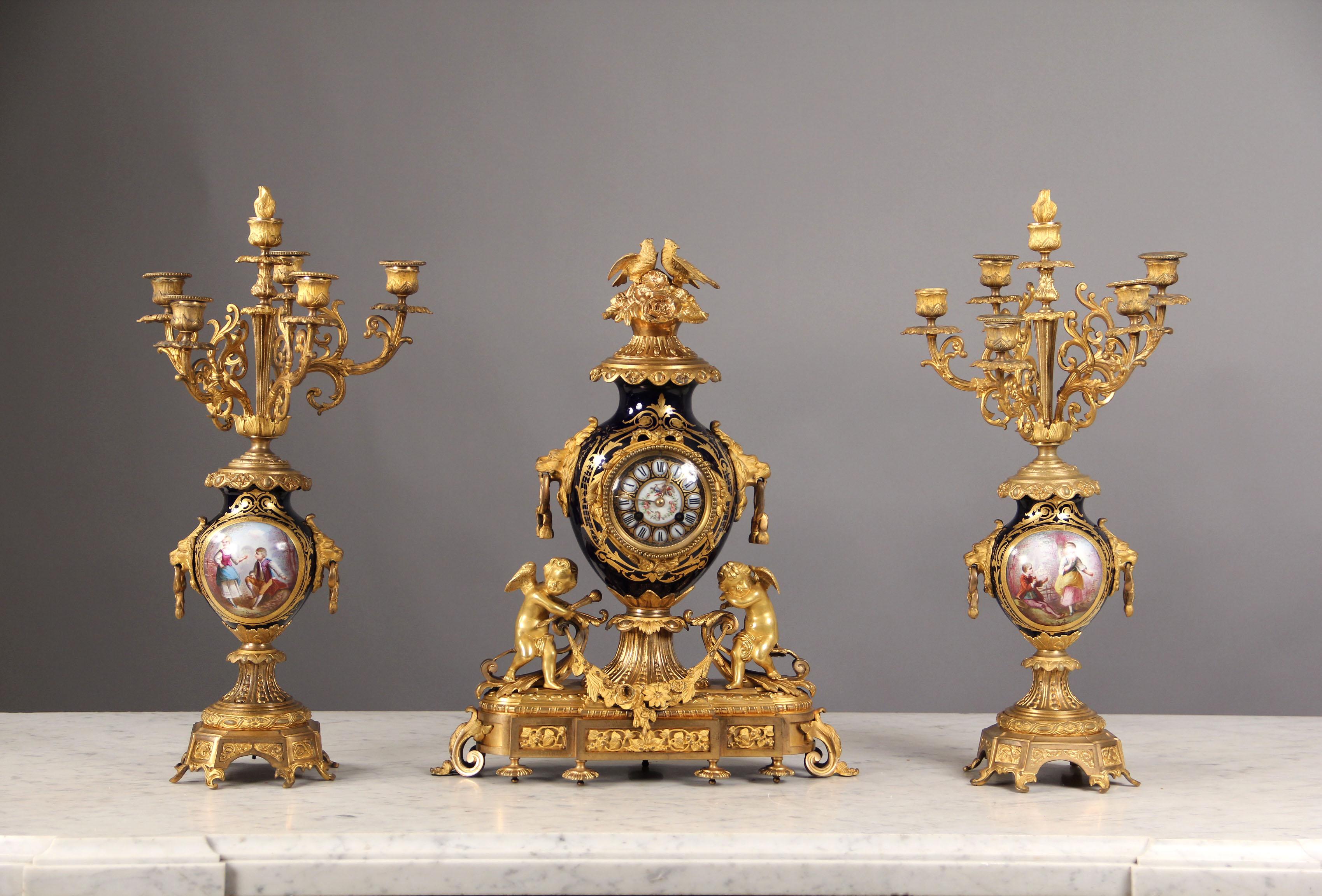 Late 19th Century Gilt Bronze Mounted Three Piece Cobalt Blue Sèvres Style Clock Set

Comprising: a round clock with a final with two birds; a pair of five-light candleabra with scrolled branches issuing from round shaped vases painted with a