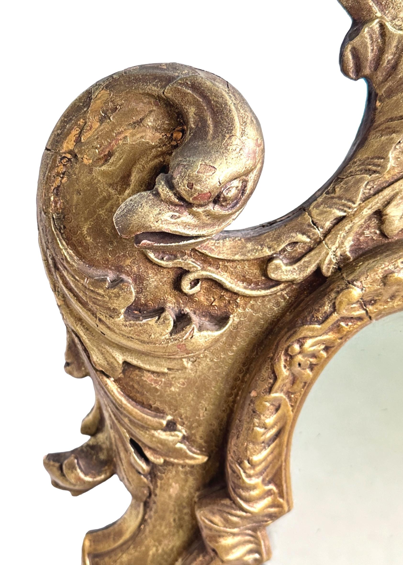 Charmant miroir en bois doré et gesso de la fin du XIXe siècle, dont la plaque rectangulaire d'origine est entourée d'un élégant cadre sculpté, orné d'aigles à volutes, de têtes de personnages grotesques et, au centre, d'un élégant panache de plumes