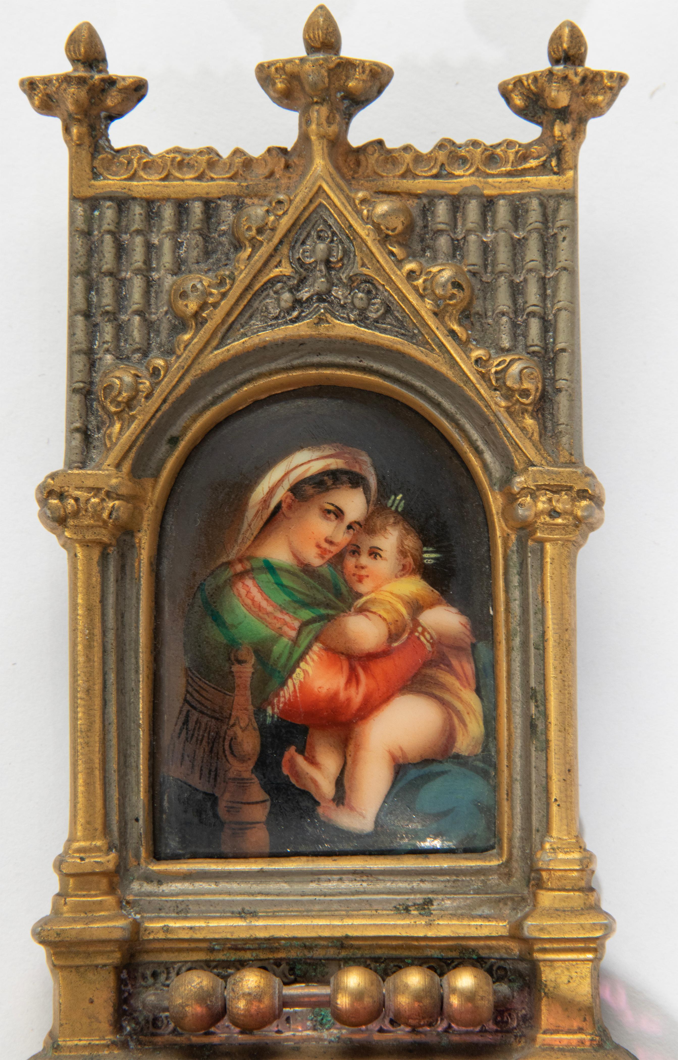 An antique holy water font in Gothic style, made of gilt bronze with a cranberry glass font. In the center there is refined hand-painted panel depicting Mary with baby Jesus, painted on porcelain. Made in France, around 1870-1880. It was the second