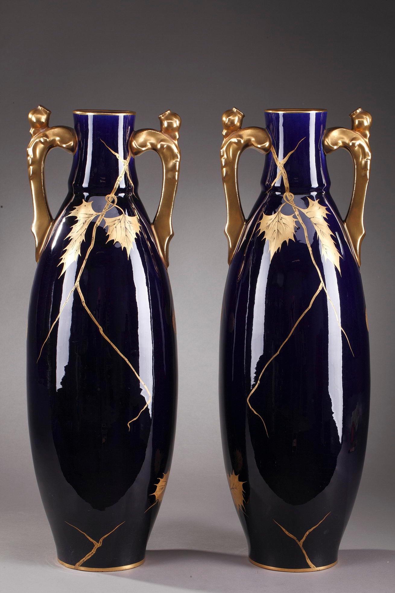 Large porcelain vases crafted by Gustave Asch in the late 19th century. Each vase is highlighted with cascading chestnut leaves and chestnuts in their bugs painted in gold on dark blue called Bleu de Tours background. The handles are entirely