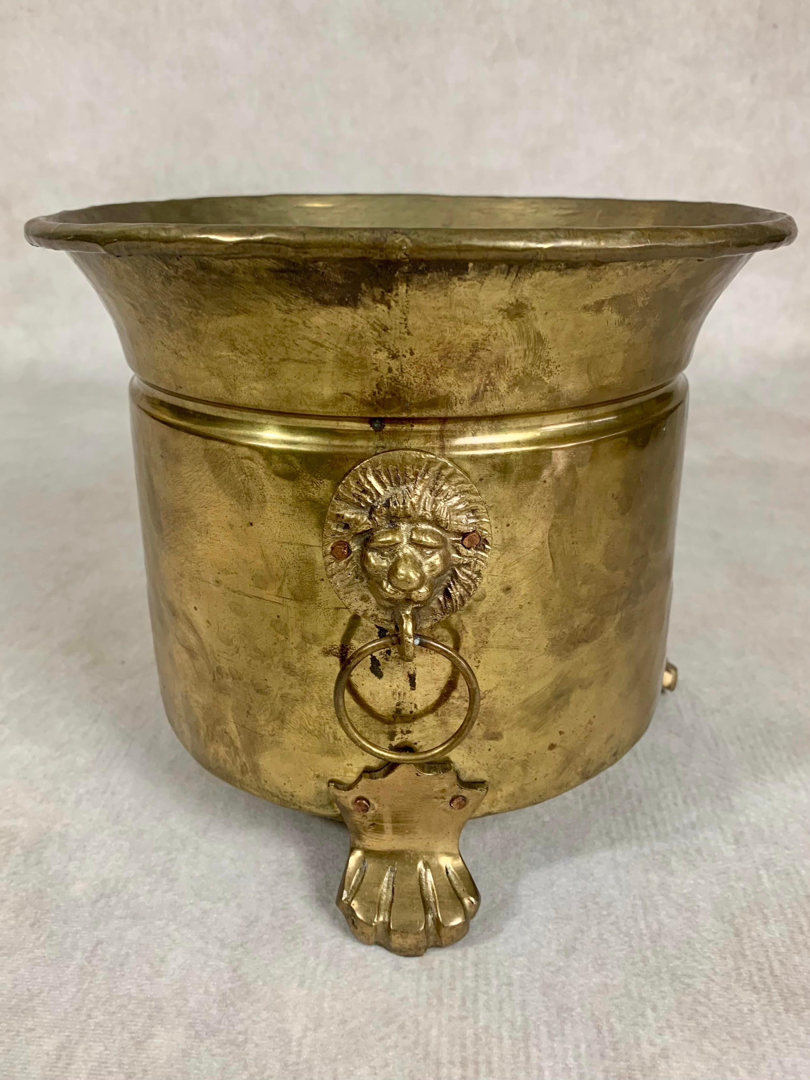 Late 19th century hammered brass jardiniere originally from France featuring lion head handles with copper rivets, a rolled rim, and three paw feet.

Normal wear commensurate with age.  Please examine photos carefully for details.