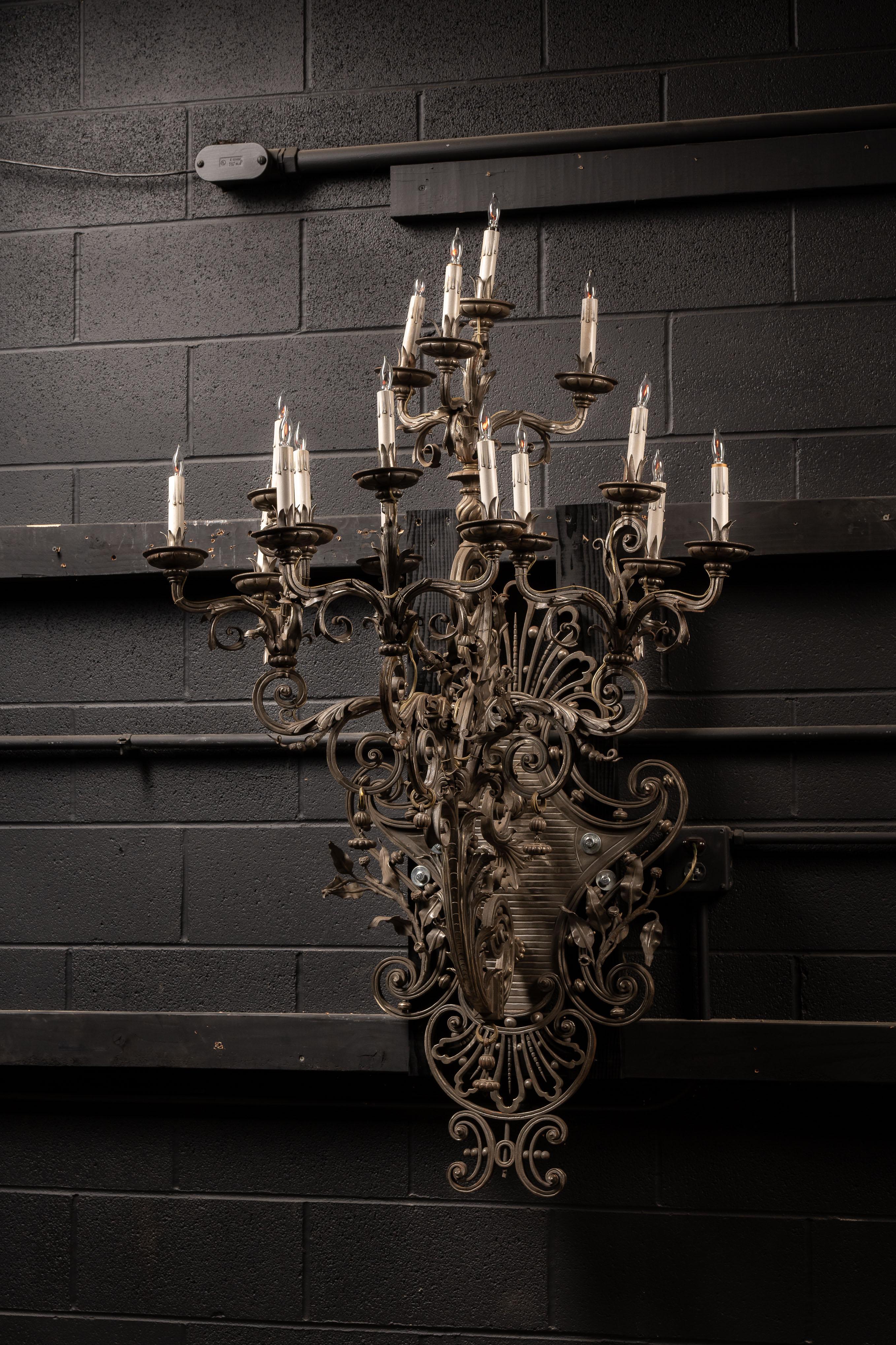 Luminaire mural en fer ancien.

Cette très grande applique est ornée de feuilles d'acanthe et d'un motif de volutes. Au dos de cette pièce se trouve une plaque décorative qui présente un aspect gaufré et nervuré.

Chacune des coupes est attachée à