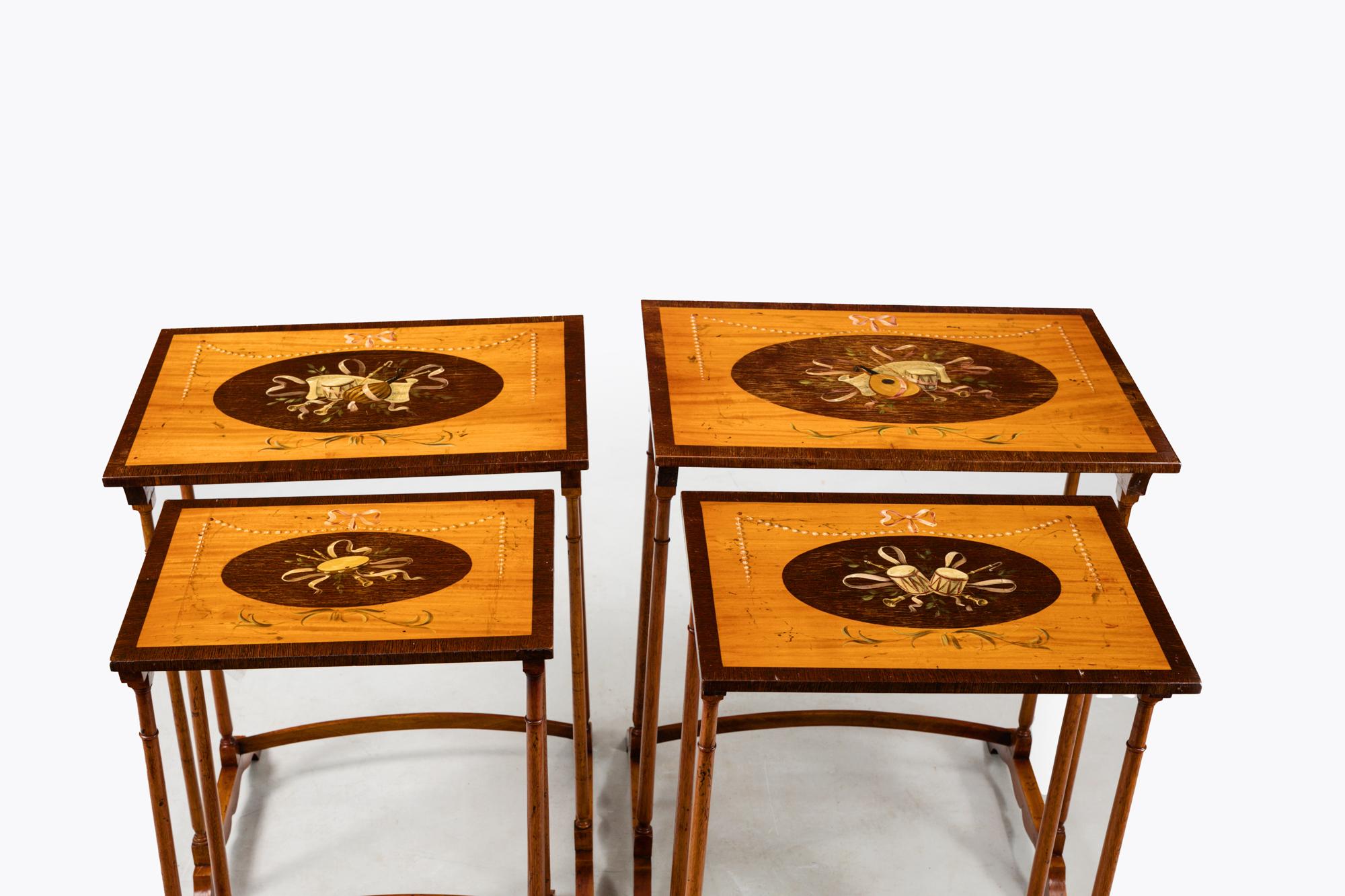 Late 19th Century nest of tables comprising of four hand painted satinwood tables crossbanded in rosewood. Featuring oval rosewood inlaid central panels. Boasting attractive hand painted designs depicting various musical instruments flanked by pearl