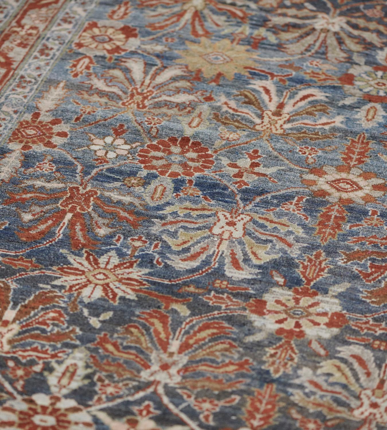This antique Malayer rug has a shaded blue field with an overall design of ivory, fox-brown and sandy-yellow palmettes and stylized flowering plants linked by a delicate floral vine, in a narrow light blue border with an angular rust-red serrated