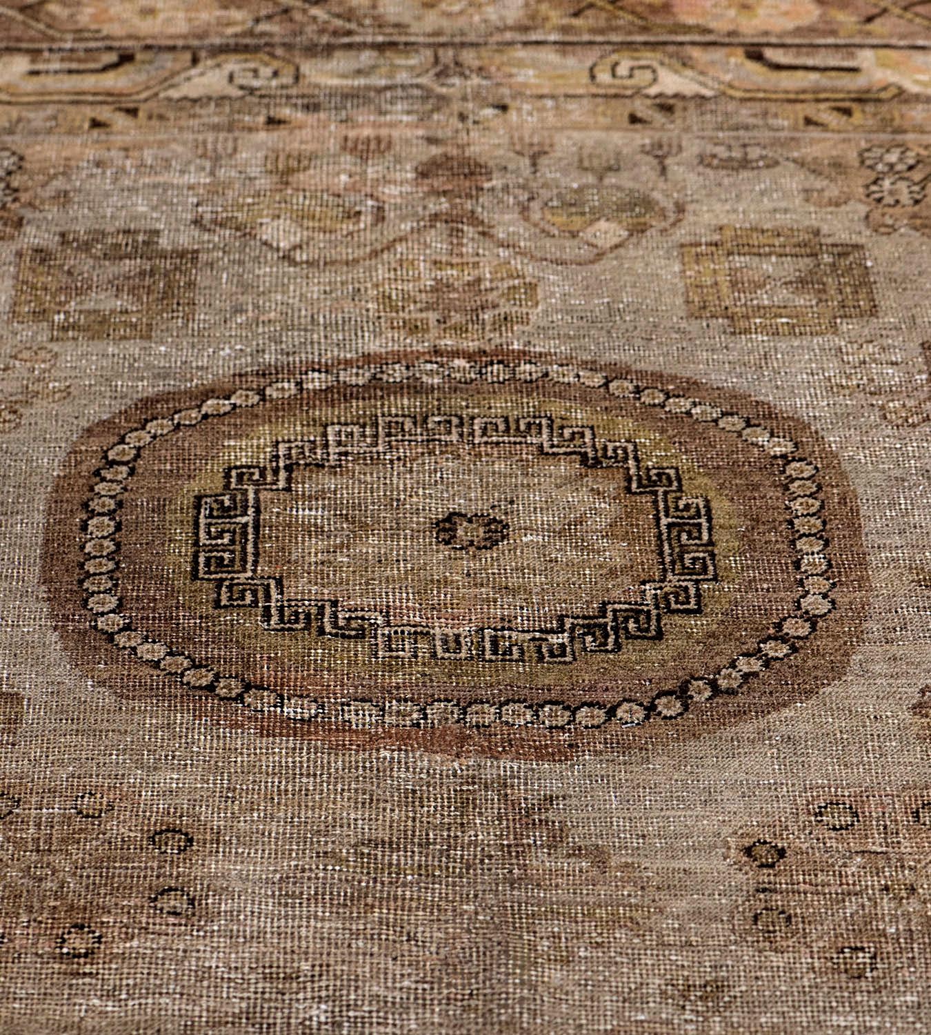 This antique Khotan rug has a stone-grey field with a central column of three roundels each containing an angular floral motif and linked circular motif bands, in a shaded soft buff-brown double border of angular linked stylised cloud motifs and