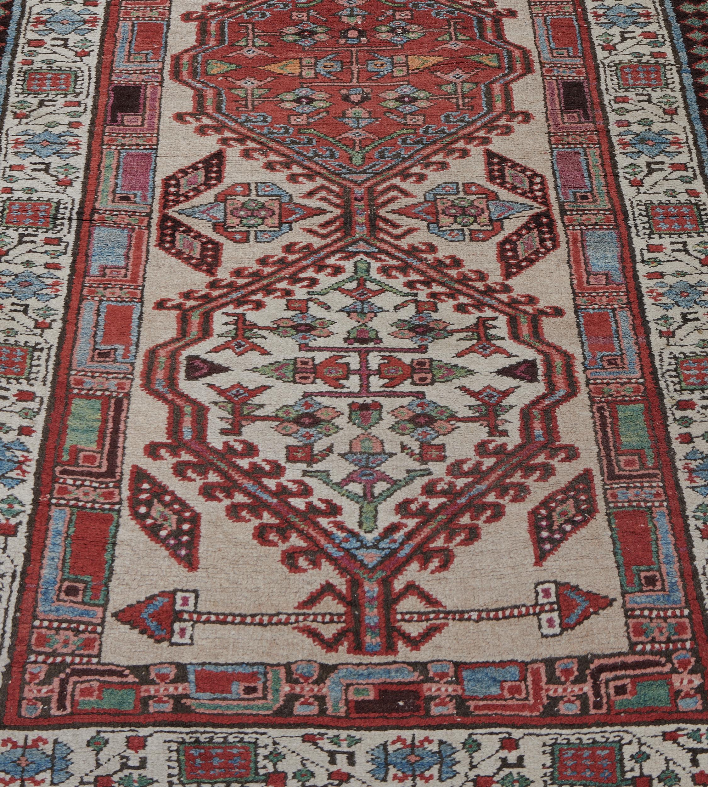 This traditional hand-woven Persian Serab rug has a shaded light camel field with alternating ivory and madder serrated lozenge medallions, in an ivory geometric floral vine border, between geometric stripes, plain outer tobacco stripe.