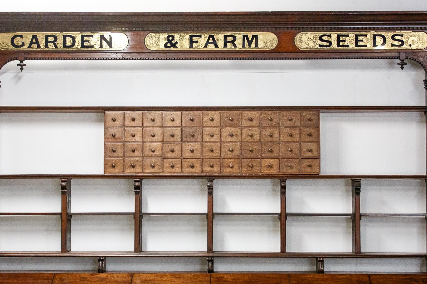 A truly spectacular English seed merchants point of sale dresser. Vast scale, reverse glass painted signage, signed F Sage and company. Intricately carved decoration throughout. Standing on a bank or 24 drawers above which sit 6 original zinc lined