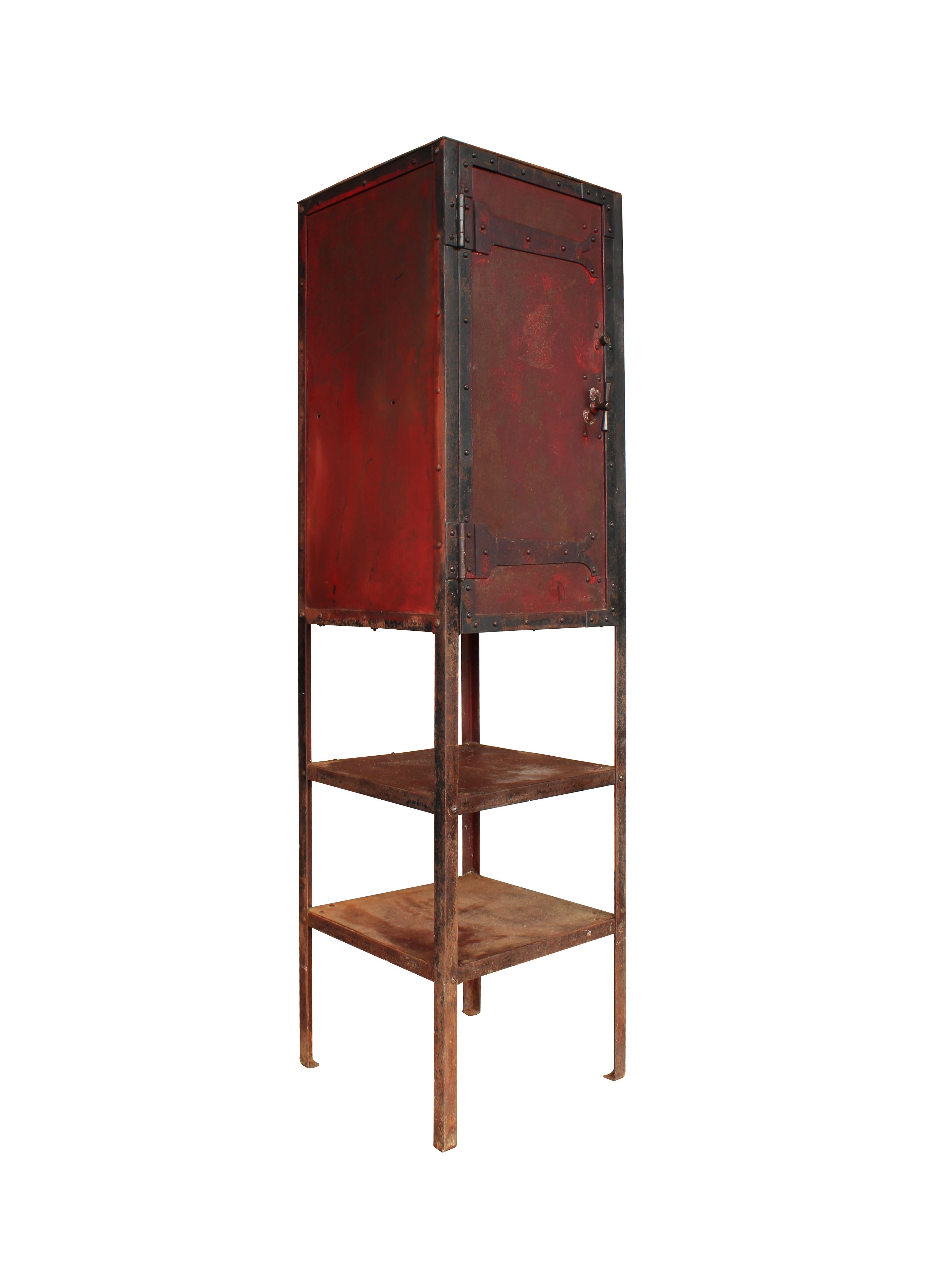This unusual freestanding Industrial cabinet is comprised of a cast iron base, steel sides featuring roughly texture red paint, and hand-forged iron T-hinges. The hinges themselves are unique in their decorative ends, which add character and beauty