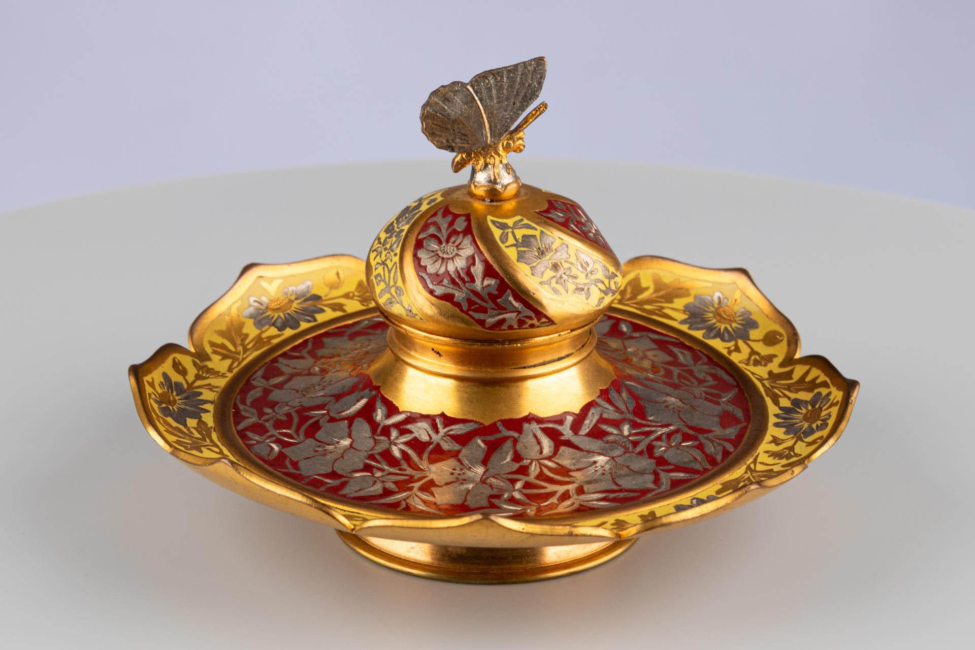 Tintero con remate de mariposa

Origen: Probablemente Francia
Material: Metal dorado con grabado floral y decoración de esmalte
Fecha: Hacia 1870-1890

Dimensiones: A × P: 11 x 15 cm

Descripción:
Este tintero, muy decorativo, presenta una forma