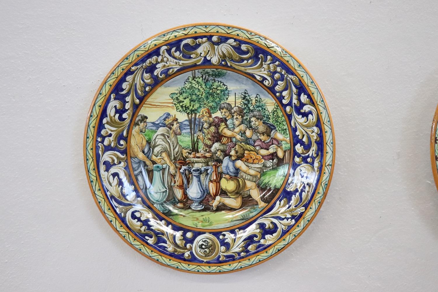 This pair of majolia decorative wall plates is beautiful and refined. Characterized by a rich decoration with bright colours. In the center animated historical scenes of ancient Rome, border decorated with spirals and leaves. Italian production from