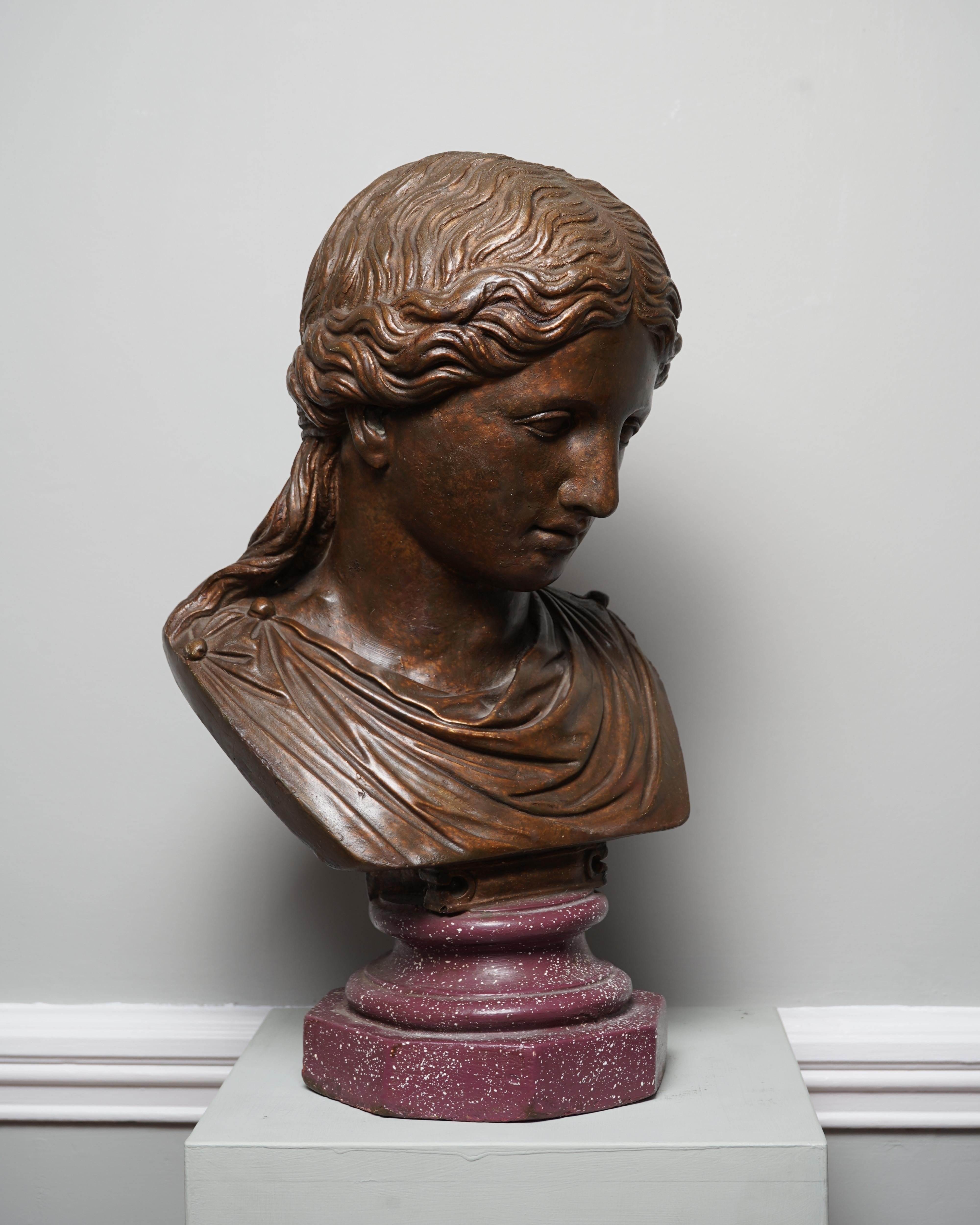 Italien, vers 1890, D'après l'antique
Plâtre bronzé et doré, socle peint en imitation de porphyre
47,5 cm. / 18.75 ins high

Ce buste décoratif en plâtre est basé sur une sculpture ancienne d'une déesse gréco-romaine classique. Buste romain restauré