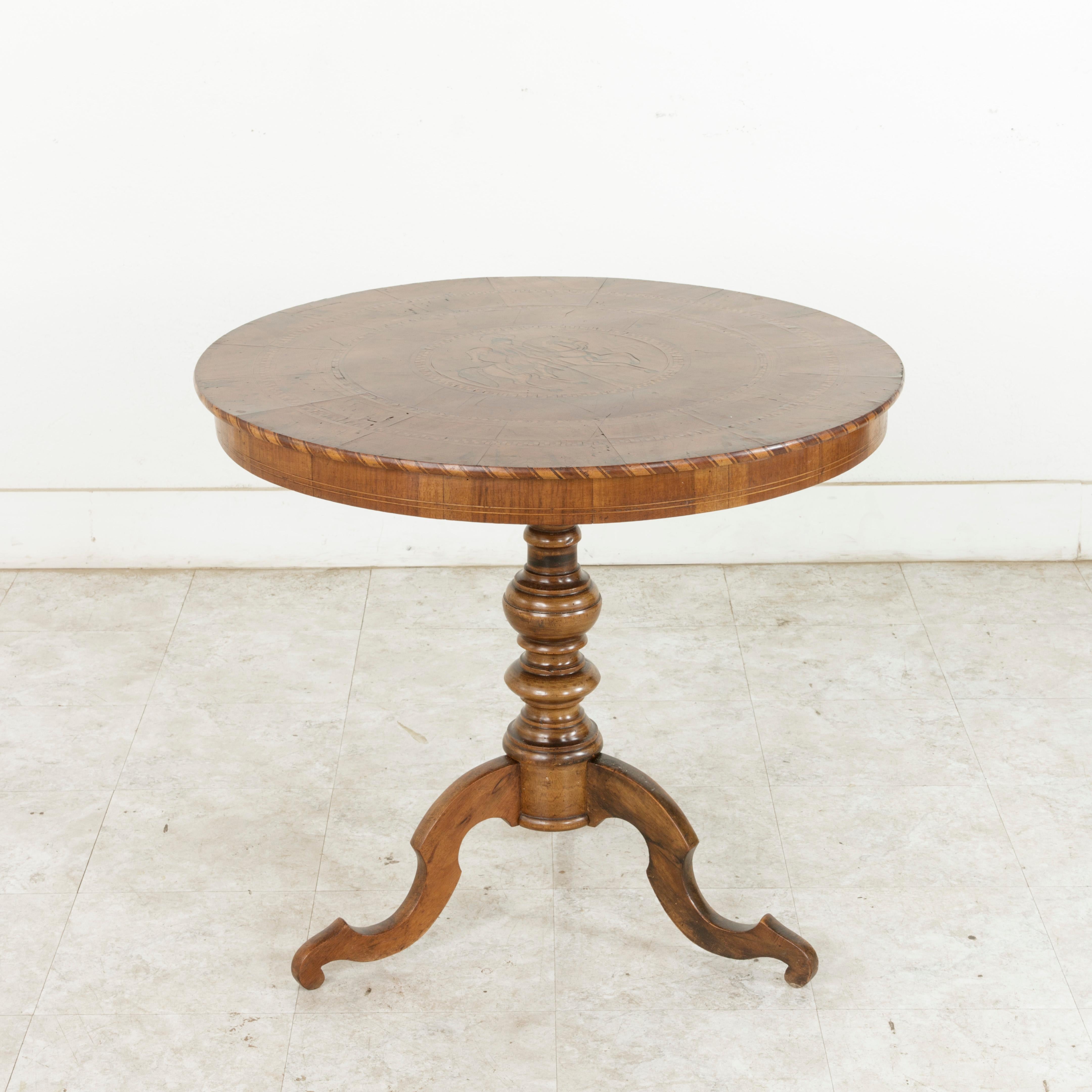 This Italian gueridon or pedestal table from the late nineteenth century features a walnut and lemon wood marquetry top with a central inlaid cavalier on horseback brandishing a lance. Concentric borders of chevron and checkered patterns encircle