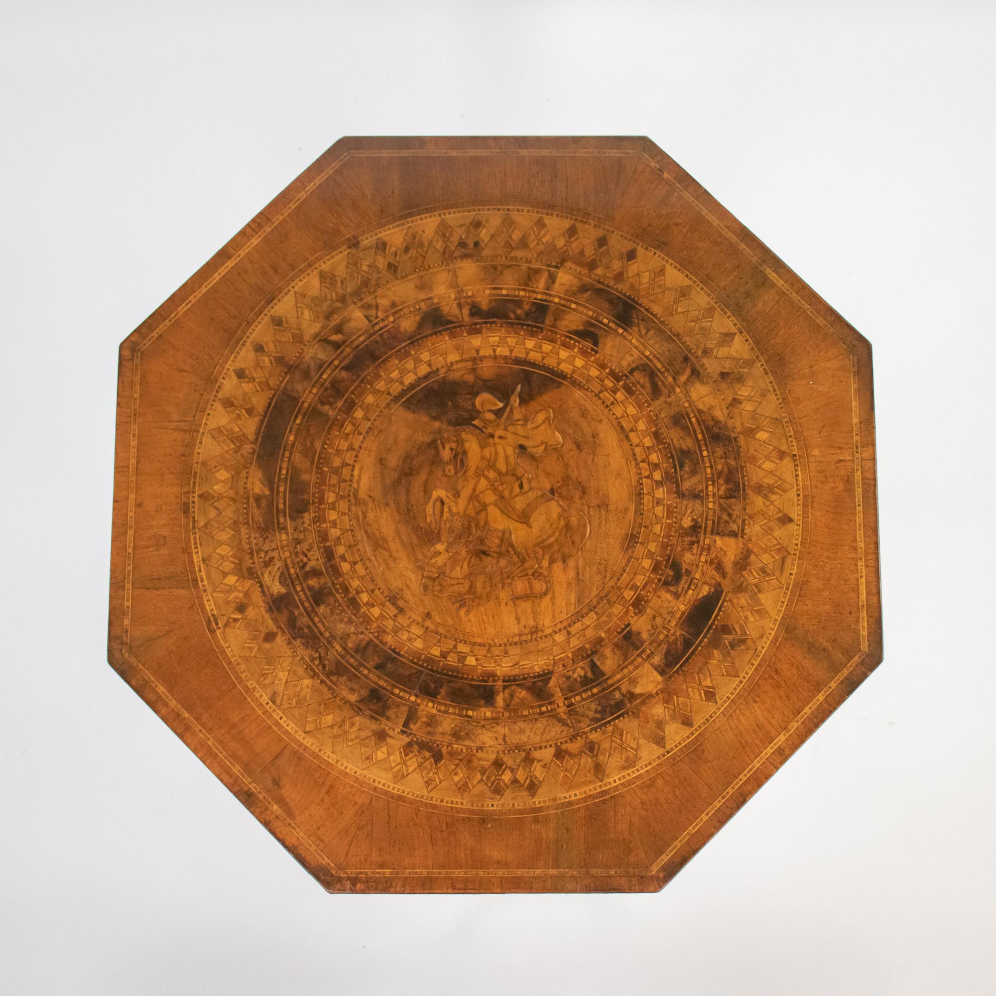Cette table octogonale, fruit de l'artisanat italien du XIXe siècle, présente un plateau en ronce de noyer richement figuré, incrusté de bandes géométriques concentriques entourant un rondeau finement détaillé représentant Saint-Georges terrassant