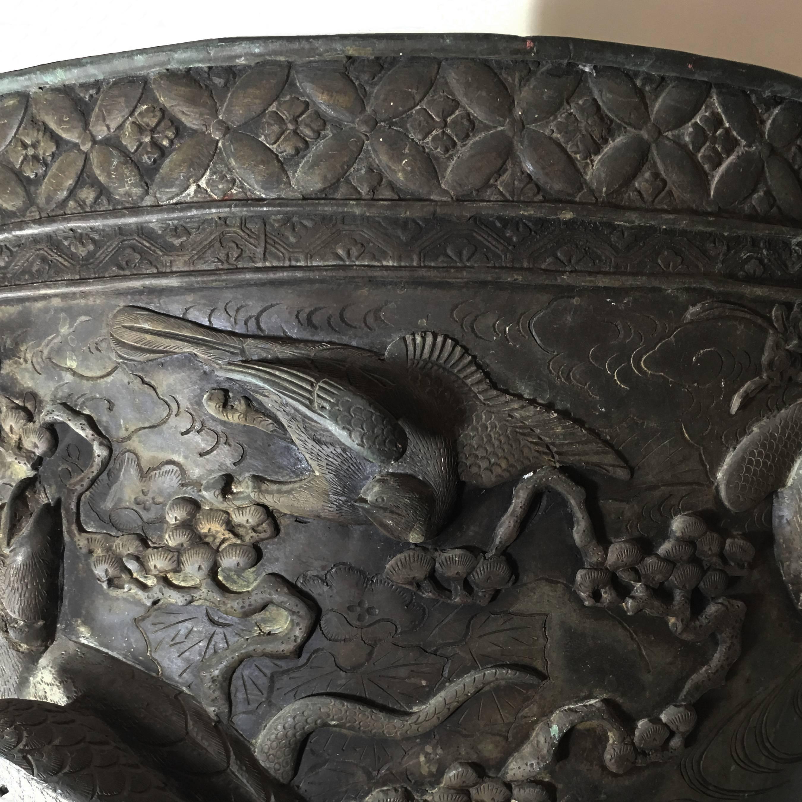 A stunning 20th century Japanese cast bronze planter or cachepot from the Meiji period. Mounted on three feet with mascherons, this antique jardinière displays a full-relief decoration depicting eagles, smaller birds and cherry tree twigs. The cast