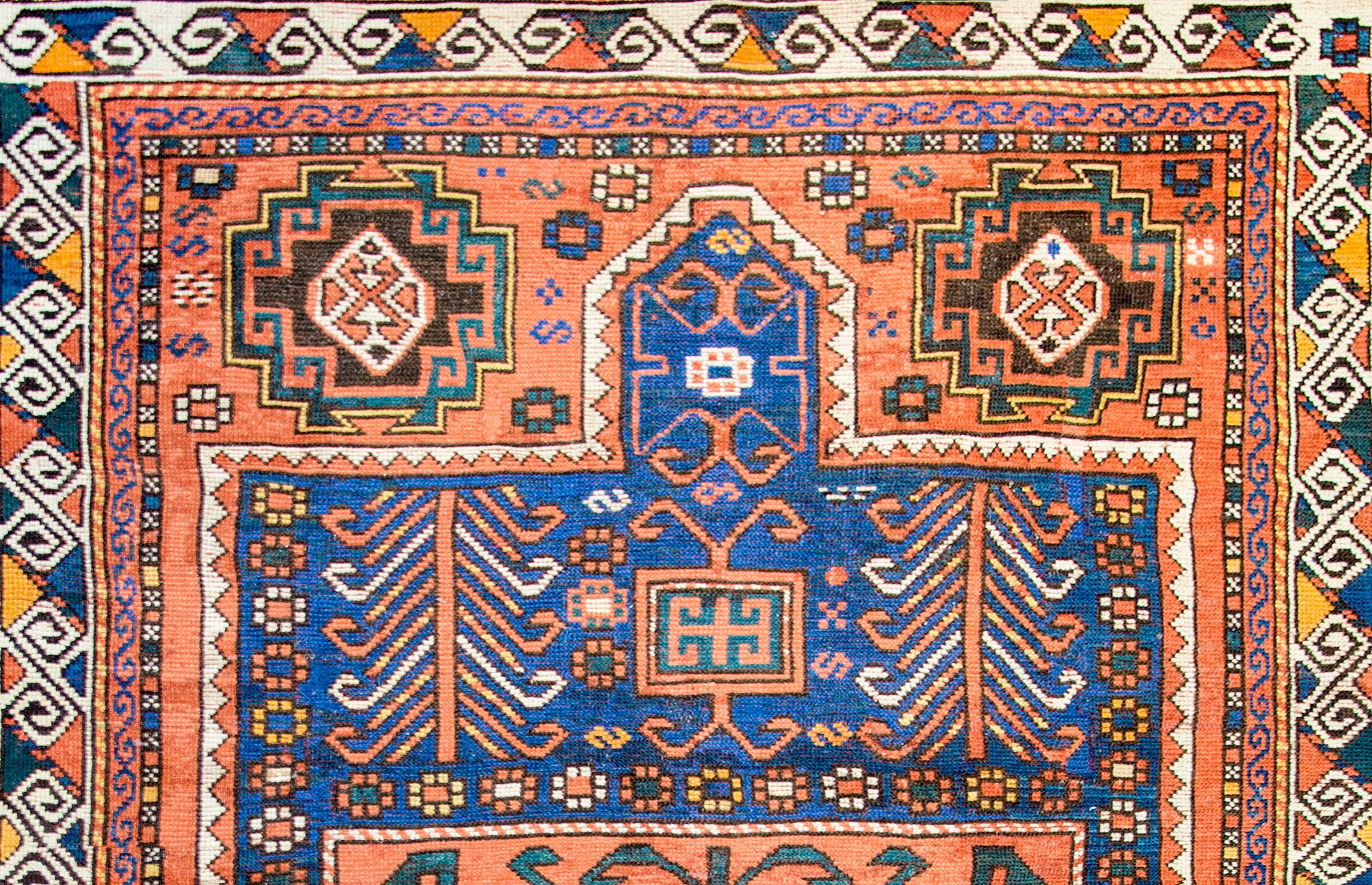 A late-19th century Kazak rug with a beautiful pattern with trees-of-life, flowers, and other geometric shapes, woven in light and dark indigo, green, brown, and gold colored wool on a brilliant crimson colored background. The border is complex with
