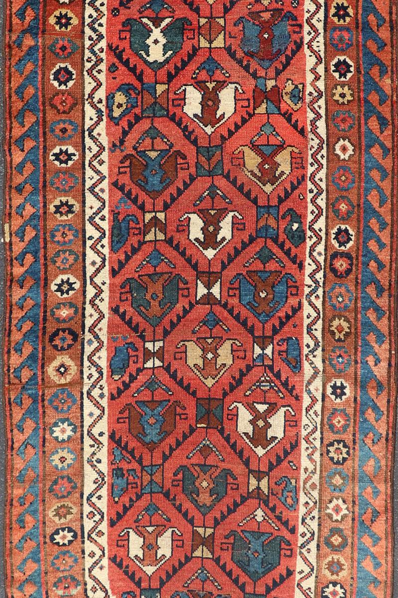 This late 19th-century treasure is rendered in red, brick, blue, ivory, sandy taupe, and small accents in salmon. The multi-tier border displays tribal-like patterns and star medallions. The field showcases large, geometric motif-like medallions.