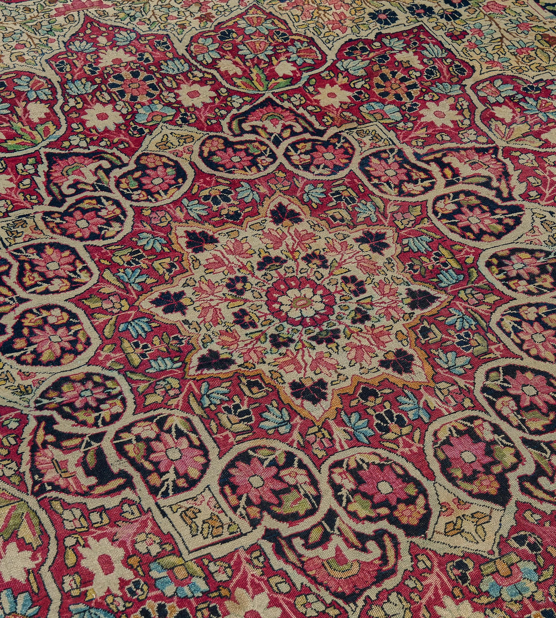 Questo tappeto antico di Kerman ha un campo avorio con una fitta profusione di rampicanti floreali policromi intorno a un grande medaglione cuspidato rosso mattone con pendenti di palmette, fitti rampicanti floreali intorno a una rosetta avorio