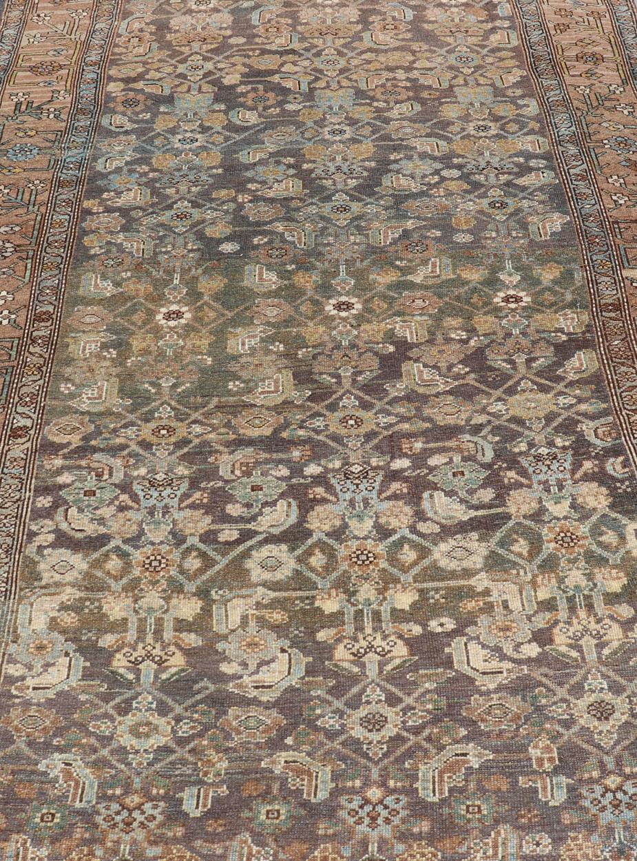 This magnificent Kurdish antique gallery runner has held timeless charm with a double-lined floral border that accentuates sandy shades of browns and light blues. The field has an all-over design featuring light blue, charcoal and other earthy tones