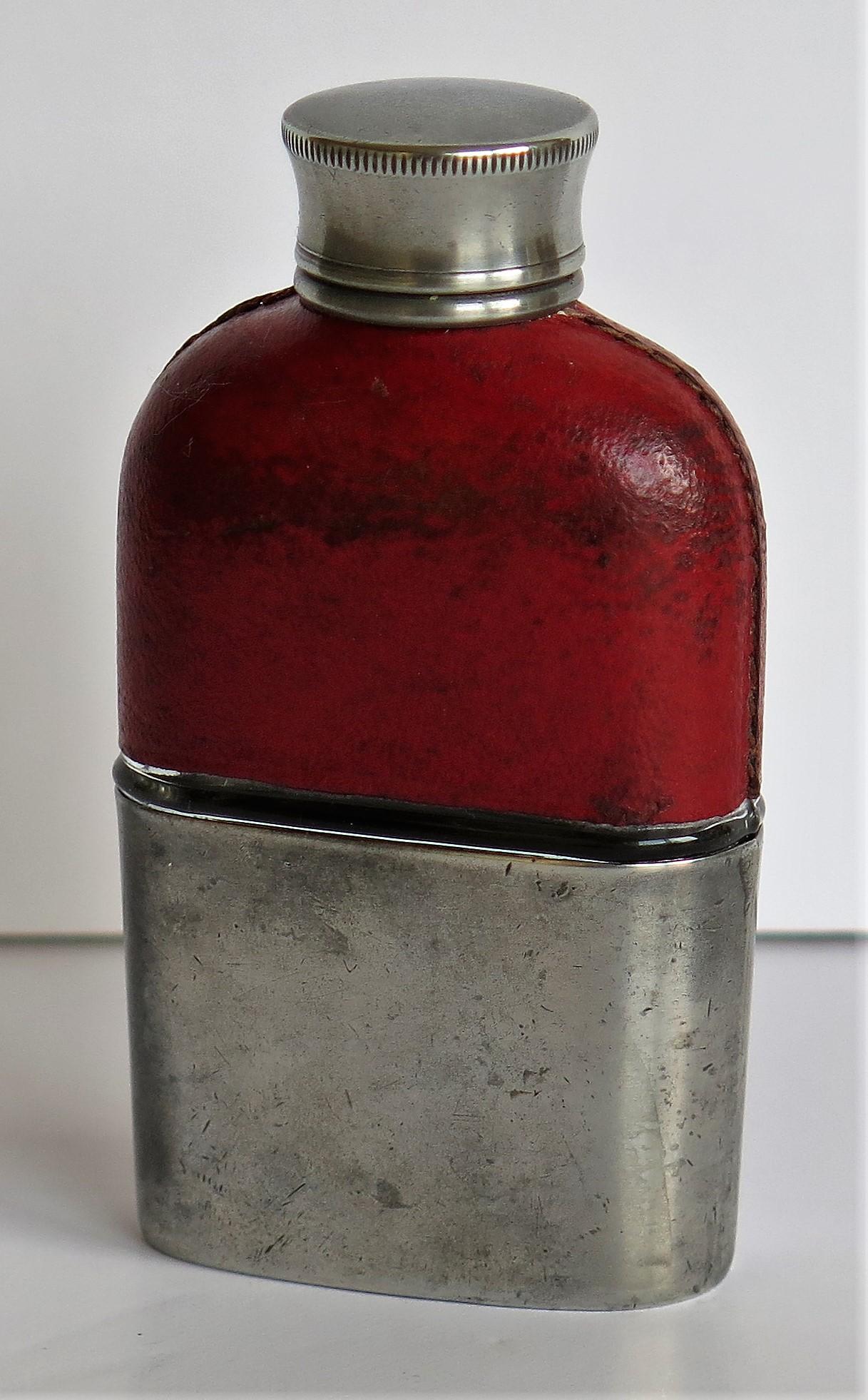 This is a small ladies antique hip flask of English make and 1.5 oz volume, dating to the late 19th century of Victorian, England.

The flask is made of moulded glass which has a red leather upper section and a pewter base, the base also acting as