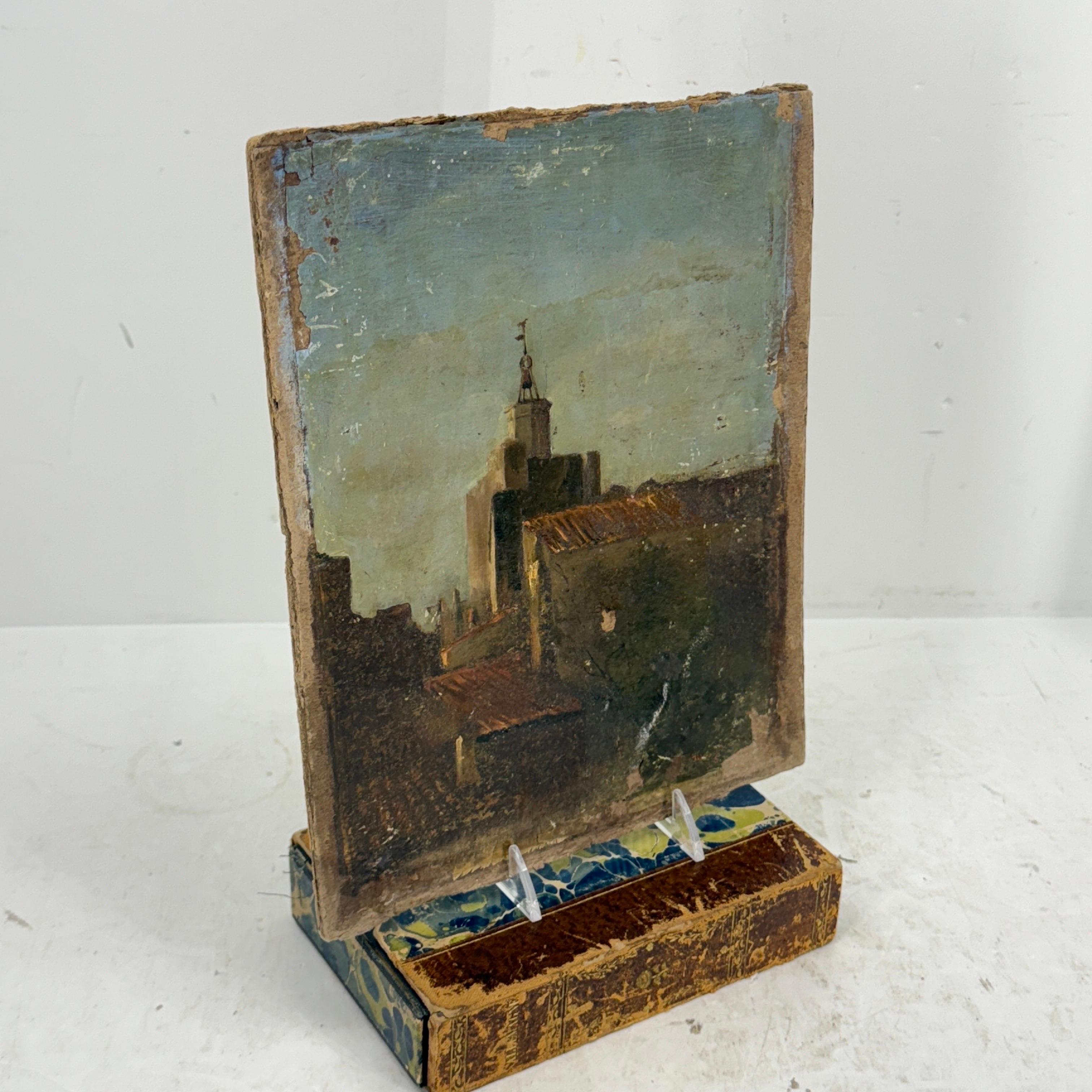 As found in a French market, a peaceful French painting on board depicting a landscape featuring a rooftop scene with houses and a building with flags in the background. Certainly, a classic piece of Parisian art to add to a collection or could