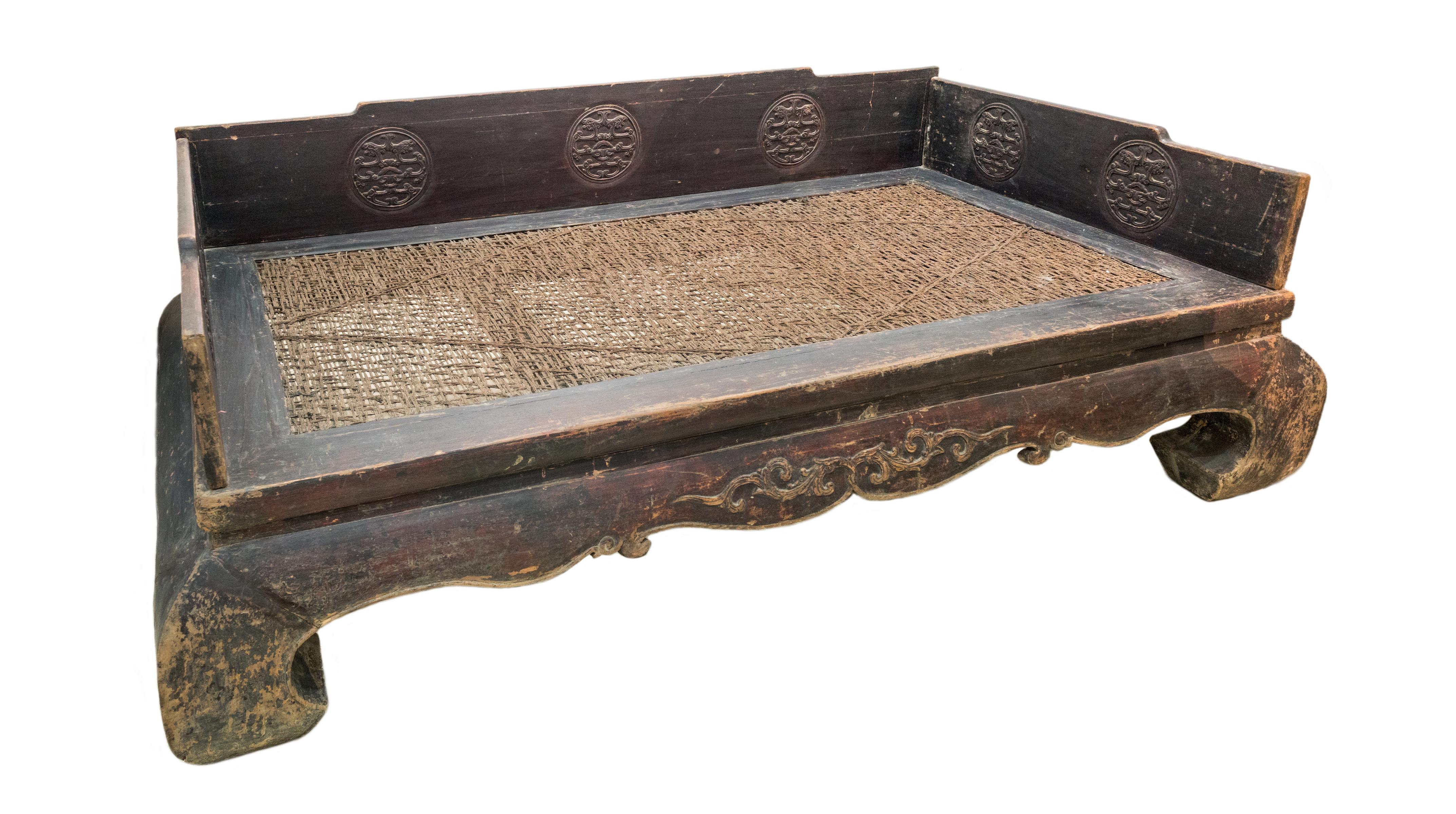 A large elmwood daybed from Shandong province, China. The color and patina of the daybed has been kept fully original, but repairs have been made to the woven seat as it was already torn. The inside of the side panels have circular carvings of the