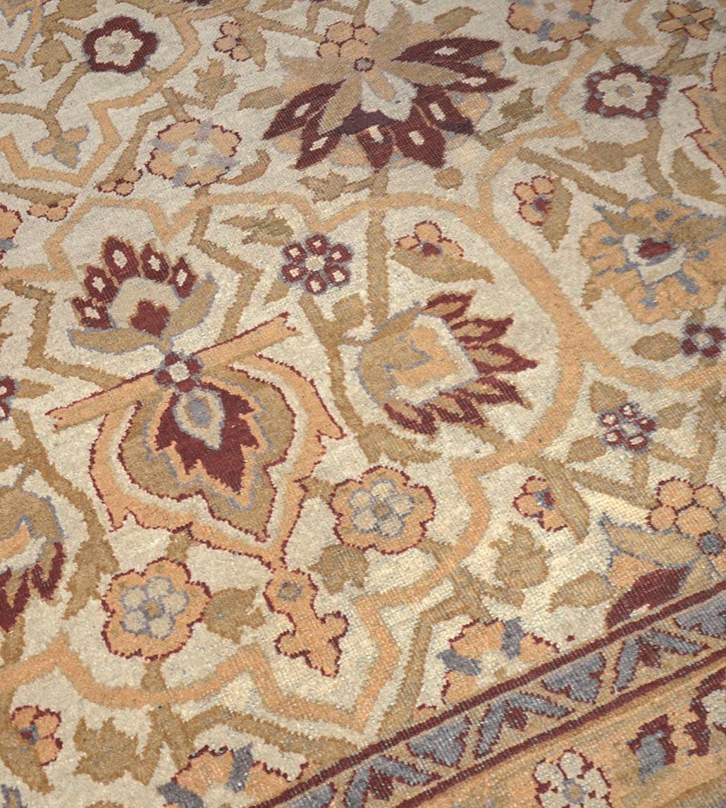 This traditional hand-woven Indian Agra rug has an ivory field with an overall design of dense scrolling vine issuing burgundy-red palmettes alternating with sandy-brown palmettes and further smaller flowerheads, in a light blue border of meandering