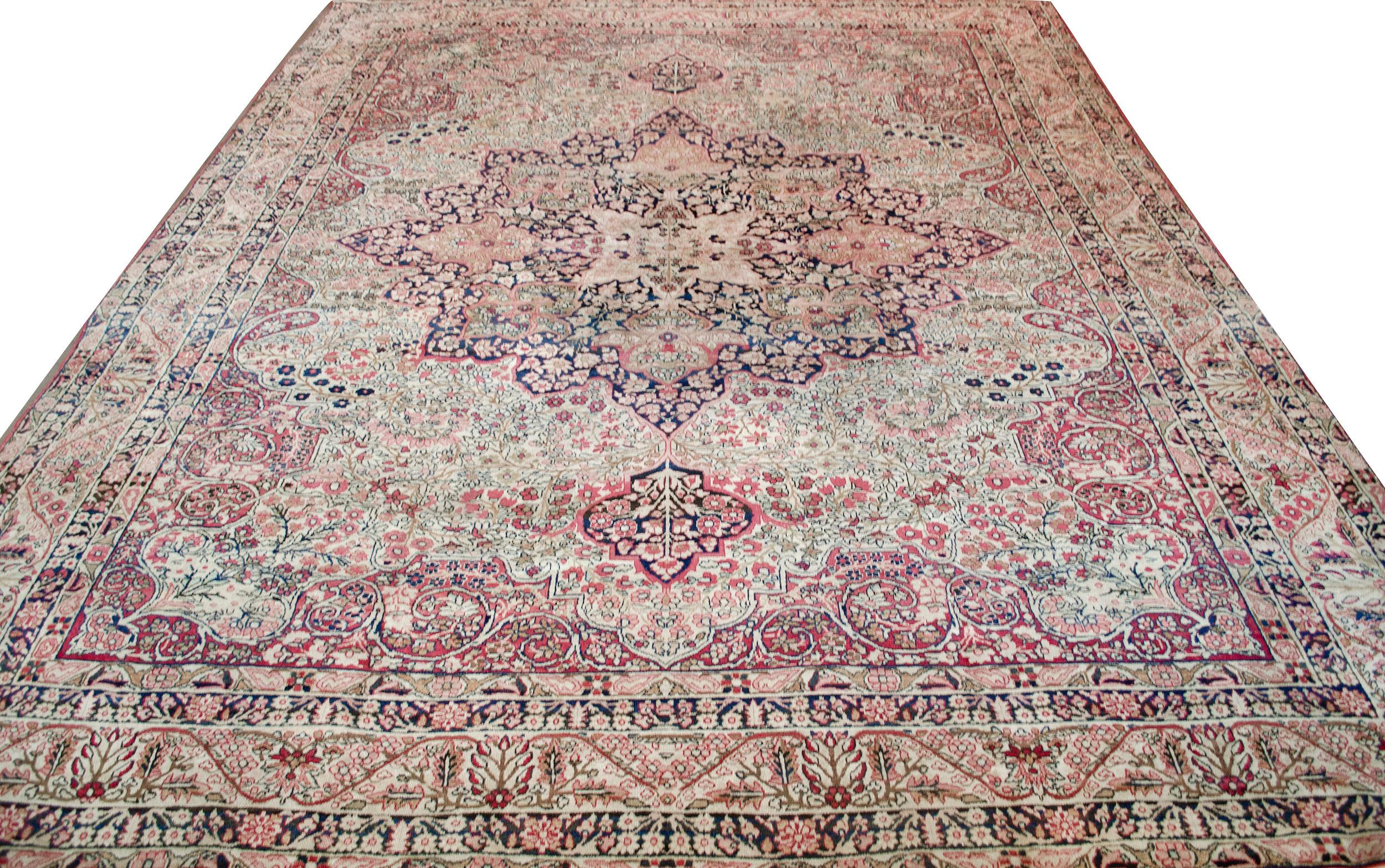 This traditional handwoven Persian Lavar Kerman rug has a gorgeous ivory cream field of dense scrolling floral vines enclosing a regal indigo radiating medallion of similar dense floral motif and radiating ornate palmettes from a central arabesque