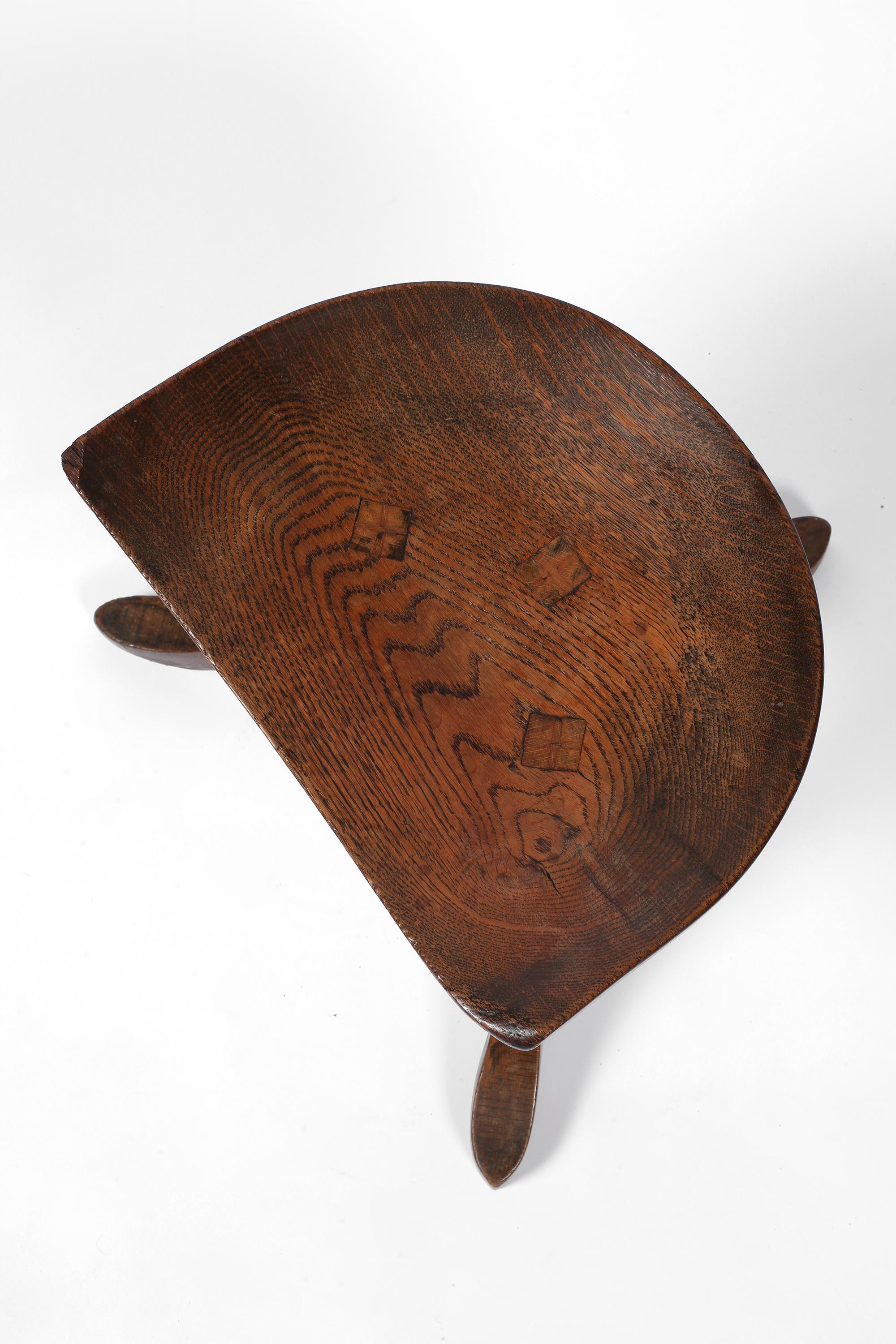 Ein perfekt patinierter, ikonischer Hocker aus geschnitzter massiver Eiche aus dem späten 19. Jahrhundert, entworfen von Leonard Wyburd und vertrieben von Liberty & Co. London. Er basiert auf einem altägyptischen Hocker aus der Zeit von 1550-1300 v.