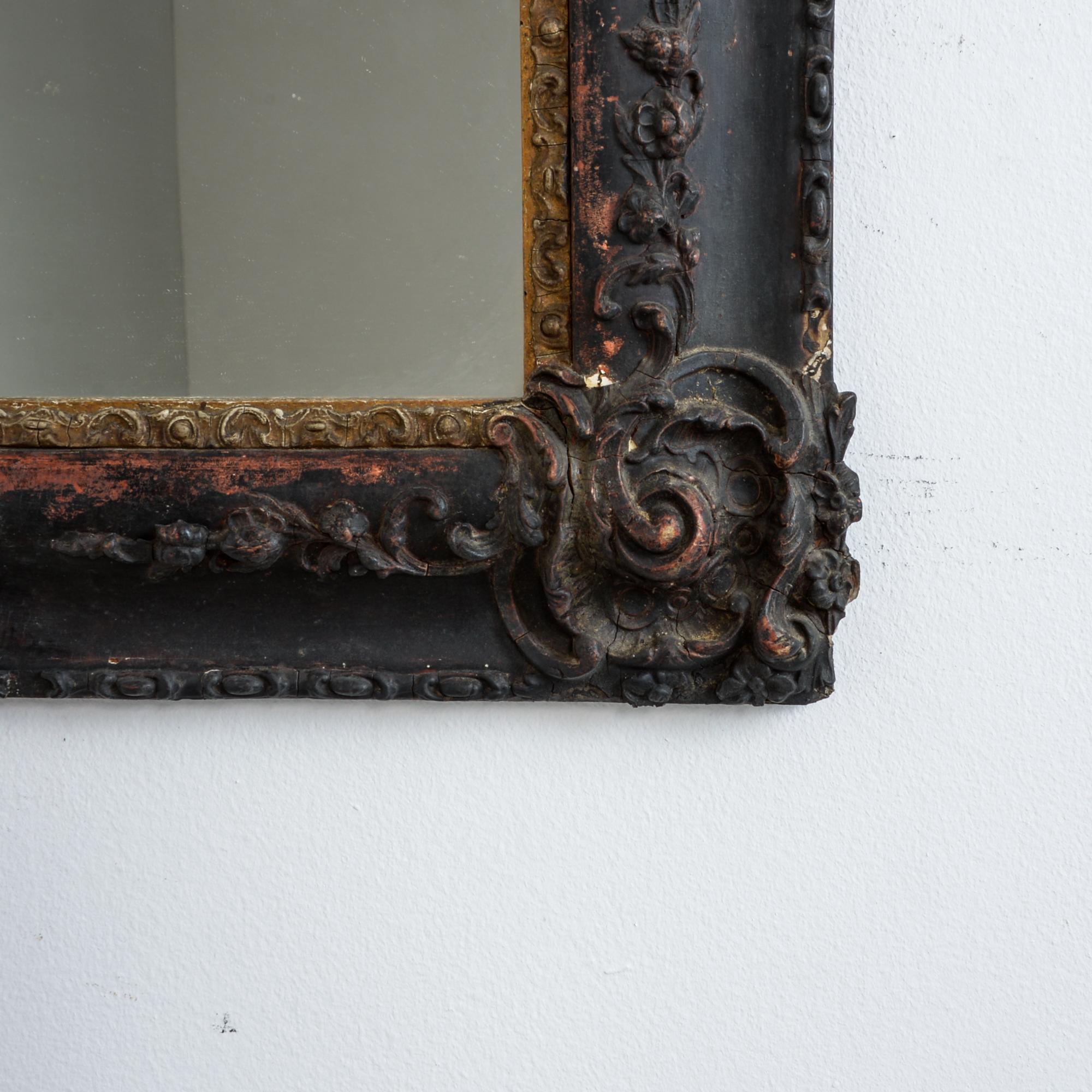 This French wall mirror has a textured patina, revealing the layers of finish for a rich and rustic effect, circa 1820. Flowers are carved and plastered in a characteristic period finishing process. An earth tone under layer has been coated with