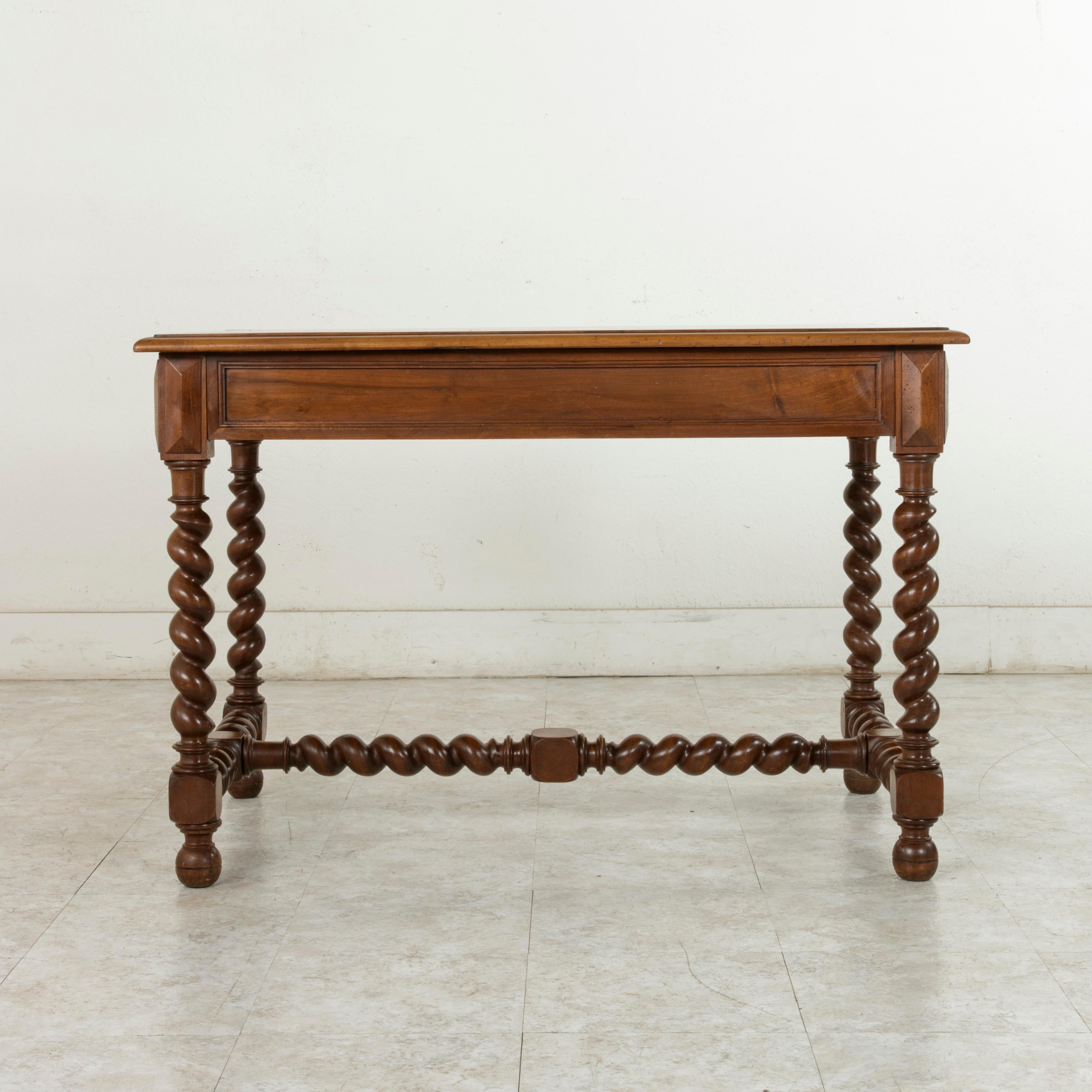 This French Louis XIII style walnut writing table or desk from the late 19th century features a beveled top supported by barley twist legs that rest on ball feet. A barley twist H-stretcher extends between the legs for additional stability. The
