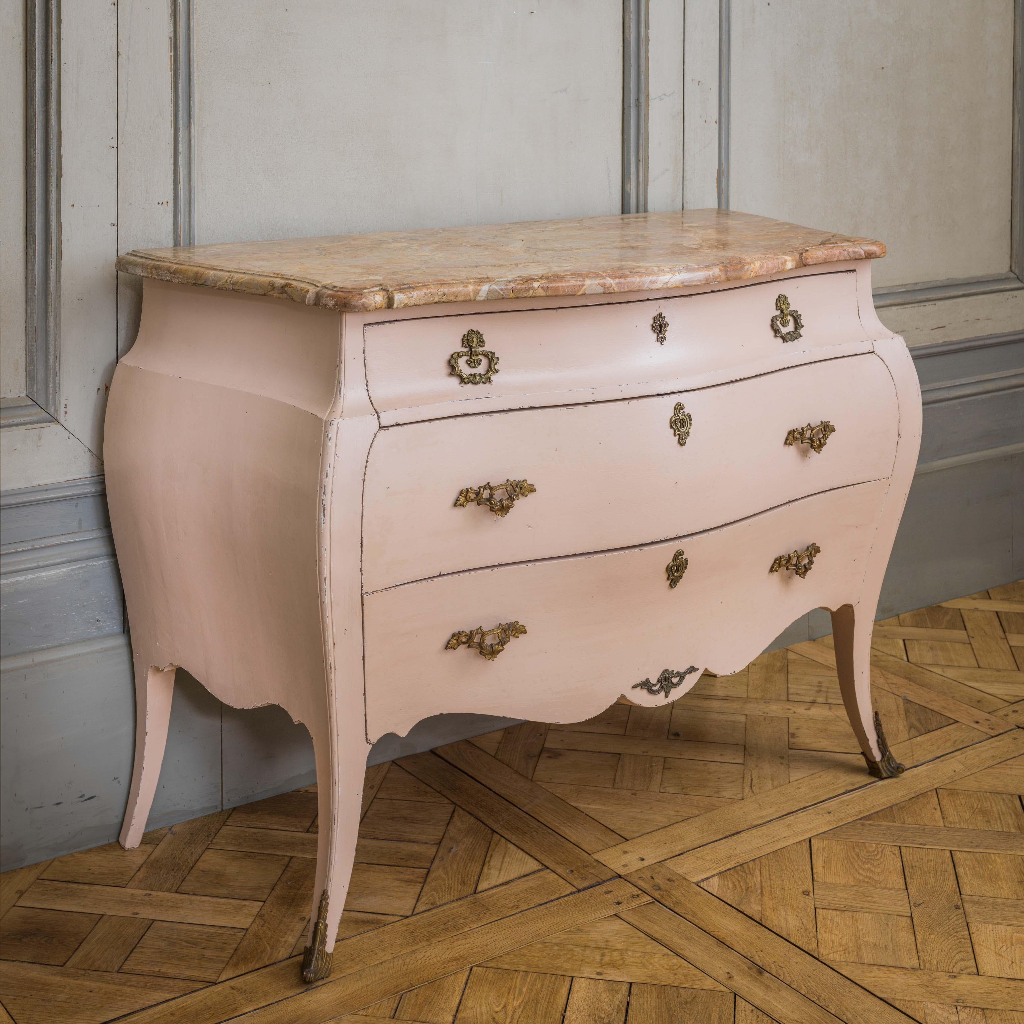 A Late 19th century Italian Bombe commode made in the Louis XV style Painted in a warm rose pink patina, with the original bronze handles and an unusual beveled marble top veined in tones of ochre.