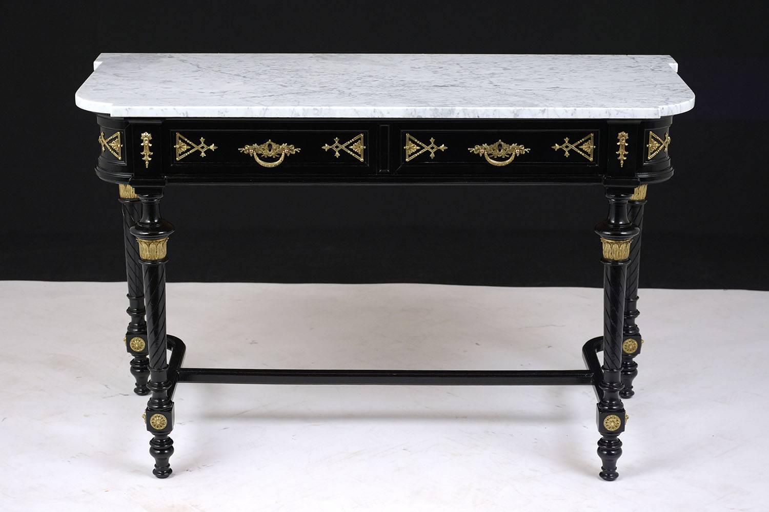 This Late 19th Century Louis XVI Console Table is made of mahogany wood with an ebonized lacquered finish and has a white marble top with grey veins. The sofa table features two top drawers with ornate brass pulls, bronze accents of acanthus