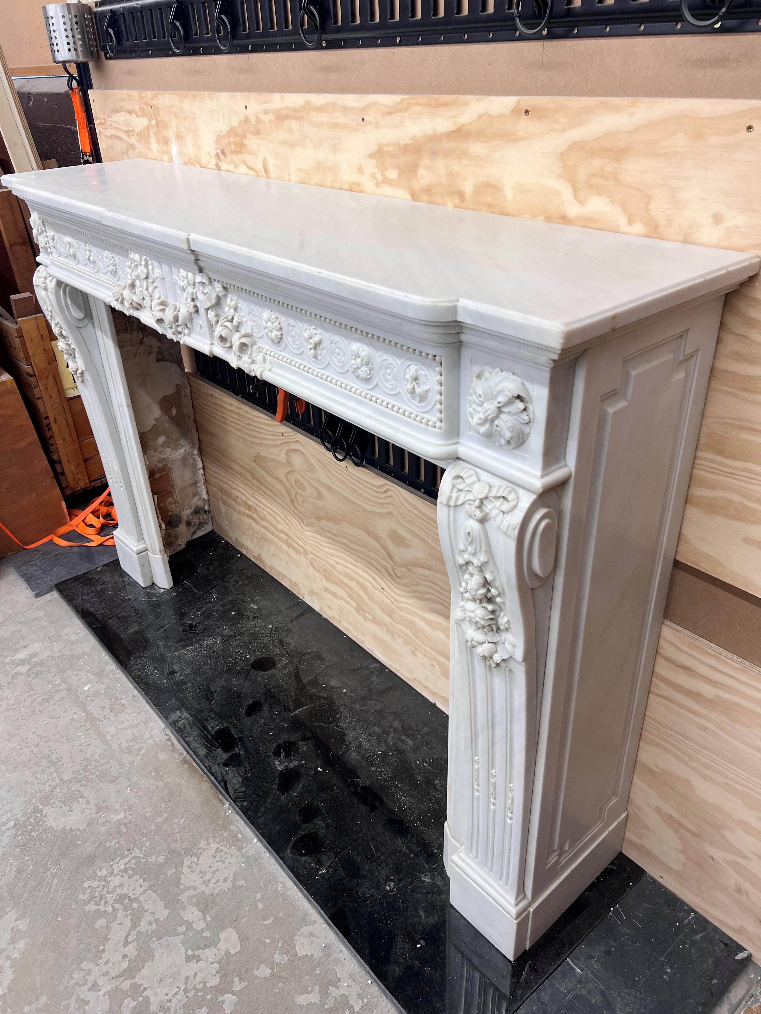 Late 19th c. Louis XVI style mantel in carrara marble with stepped frieze elaborated with guilloche carving detail, stop fluted tablet and rose swag. Fluted console jambs exhibit ribbon and rose carving details and support corner blocks with