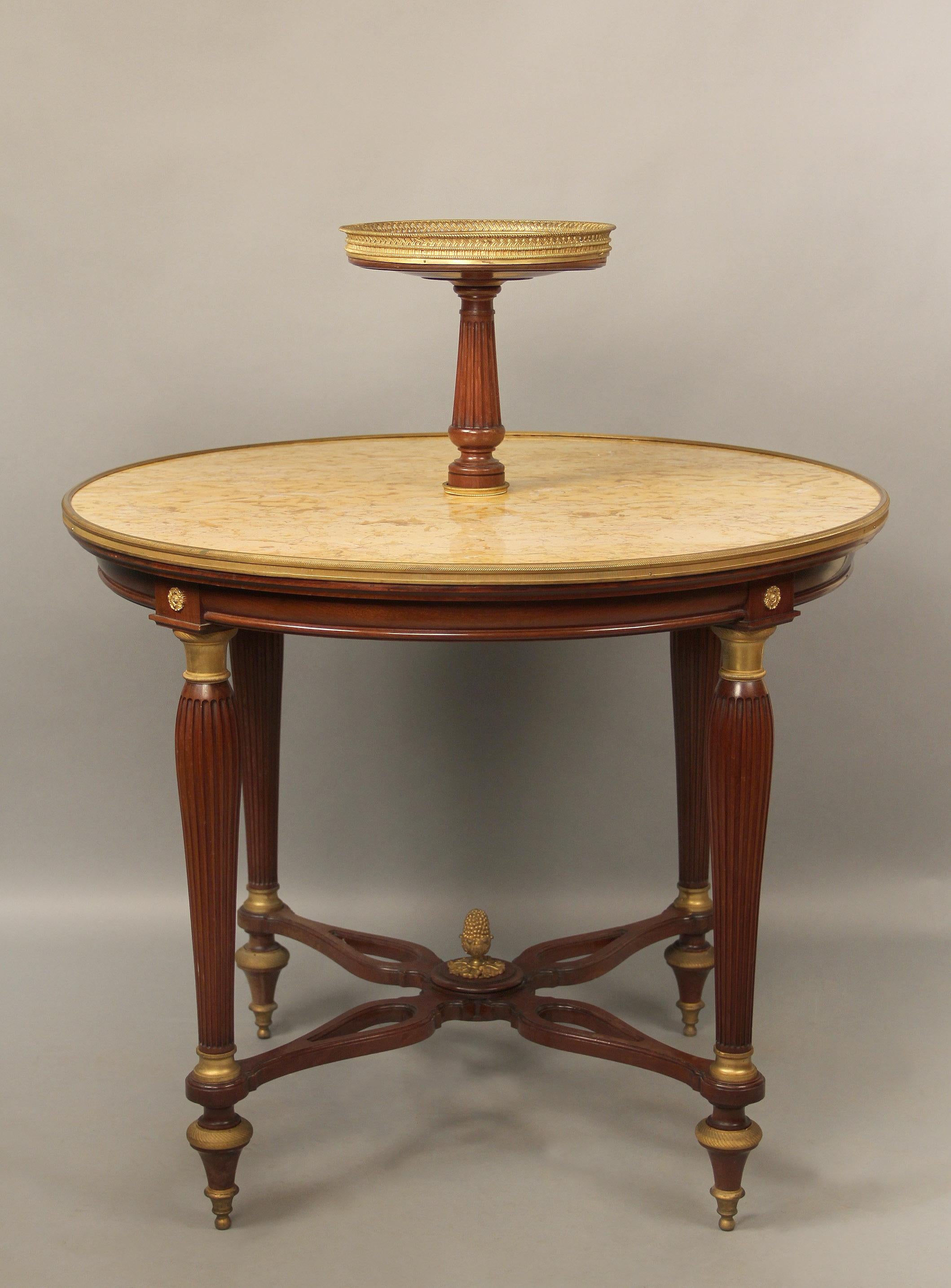 An interesting late 19th century Louis XVI style gilt bronze-mounted two-tier pastry table

Round marble-top table centered with an upper tier with a pierced bronze rim, the four carved legs centered by a bow shaped stretcher with a bronze