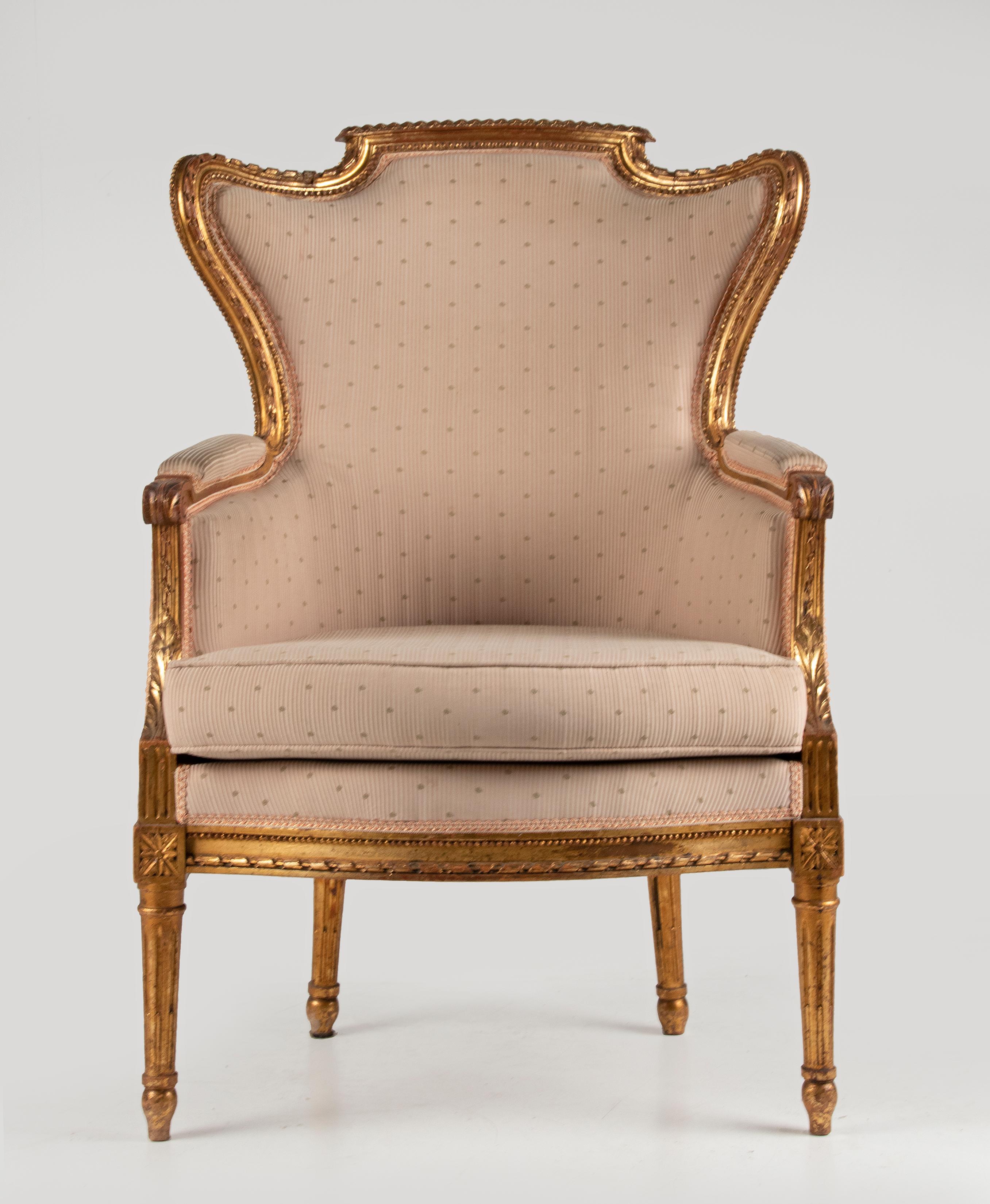 A comfortable Bergère wing chair in Louis XVI style. The chair is made of walnut and patinated with gold paint. Refined carvings, with ribbons, beading rim, acanthus leaf and rosettes. Made in France, circa 1880-1890.